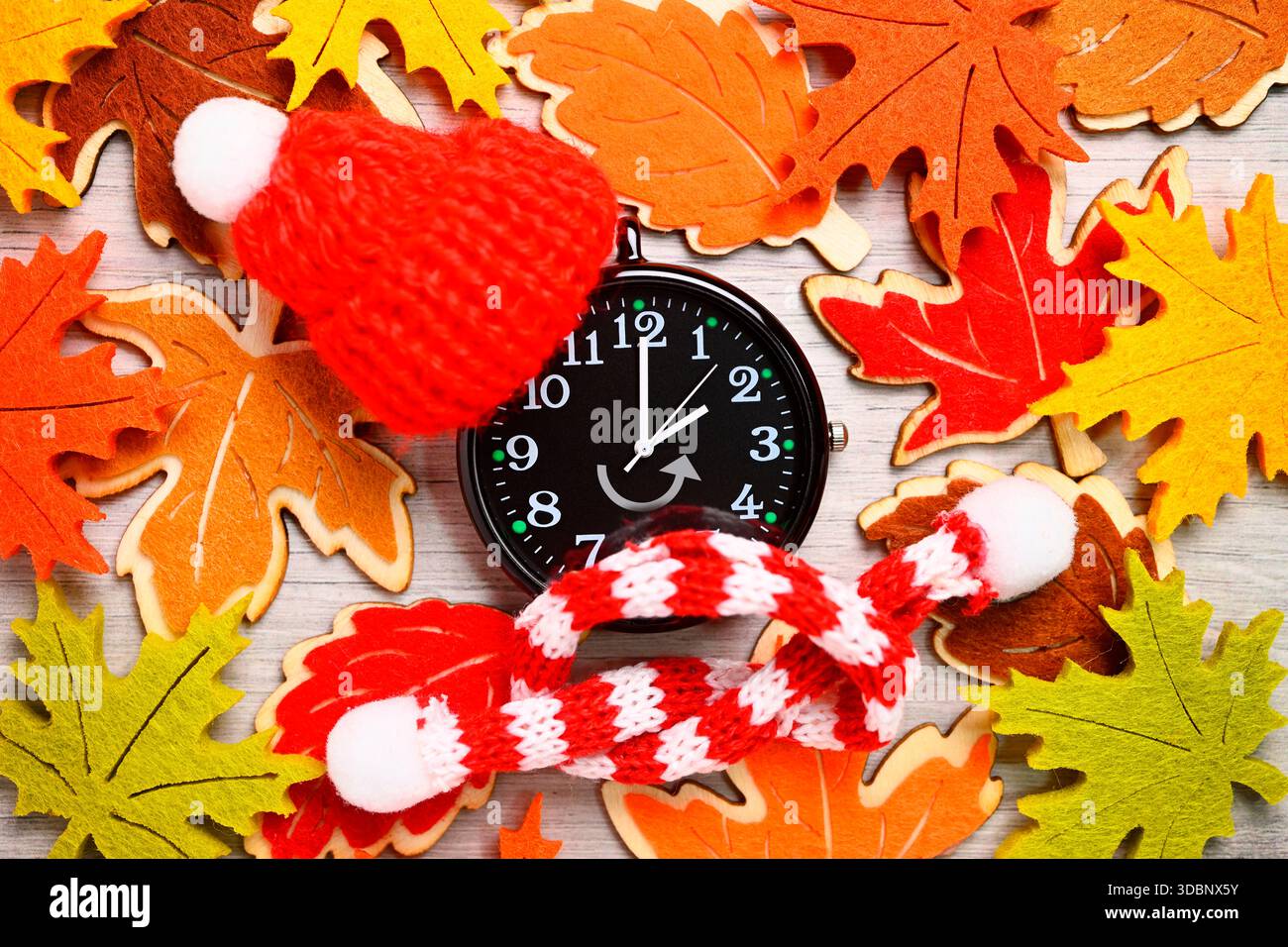 Schwarze Uhr mit Hut und Schal, symbolisches Foto von Zeitwechsel und Winterzeit, Fotomontage Stockfoto