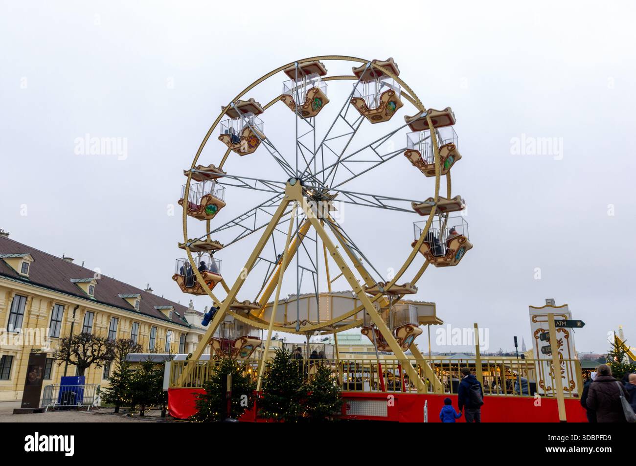 Riesenrad im Vintage-Stil am Wiener Schloss Schönbrunn an einem bewölkten Wintertag im Freien mit geschmückten Kabinen und umliegenden Gebäuden Stockfoto