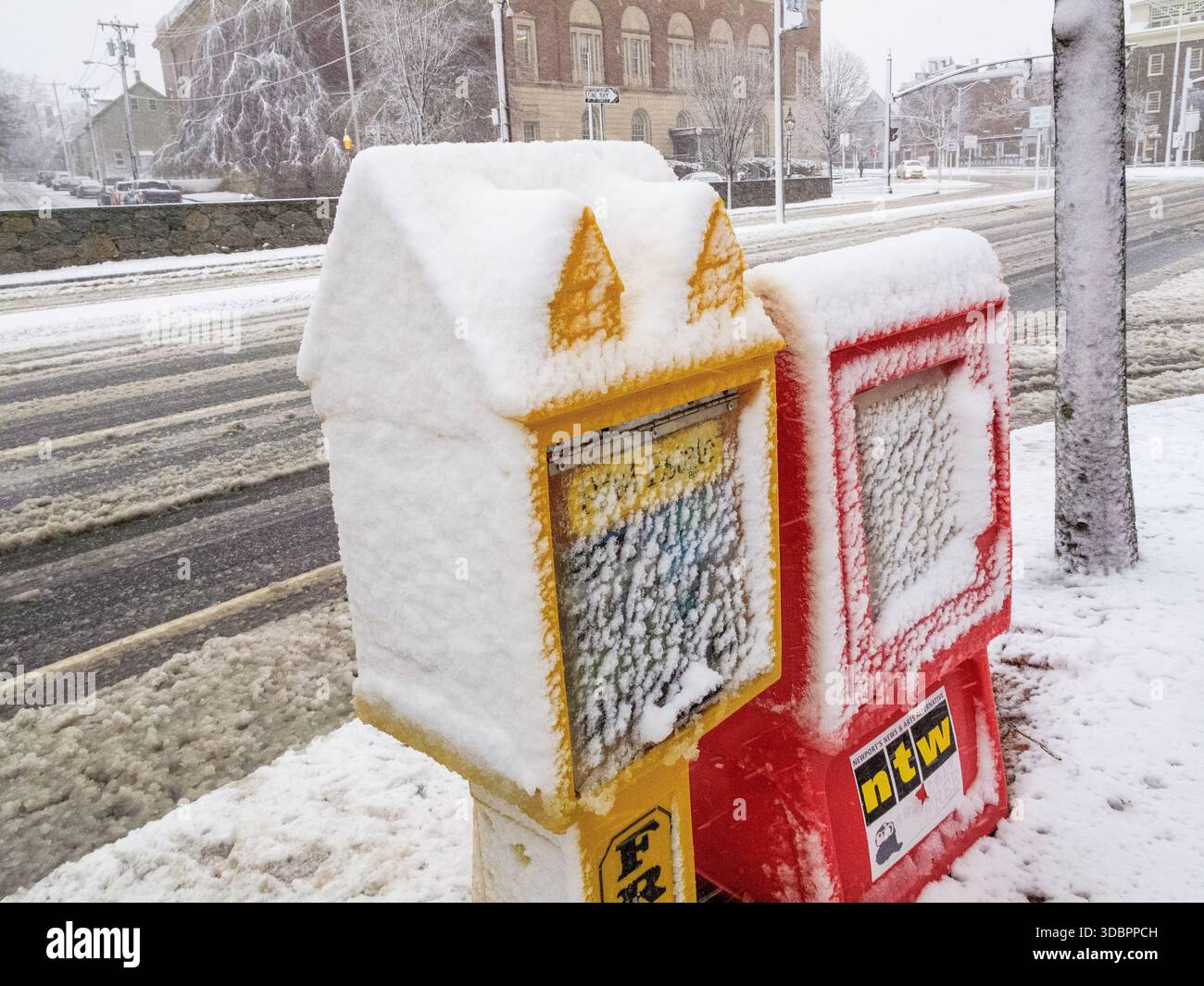 Zwei Zeitungskisten sind mit Schnee bedeckt. Eine ist gelb und die andere rot. Der Schnee stapelt sich auf den Postfächern Stockfoto