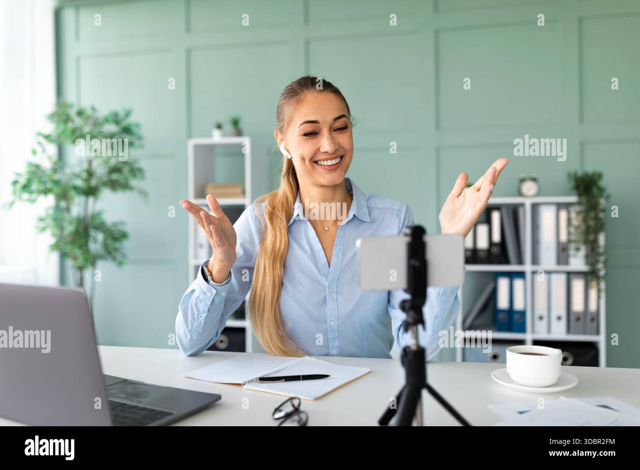 Happy Teacher führt von ihrem Office Workspace aus ansprechende Online-Lektionen mit Smartphone und Laptop durch Stockfoto