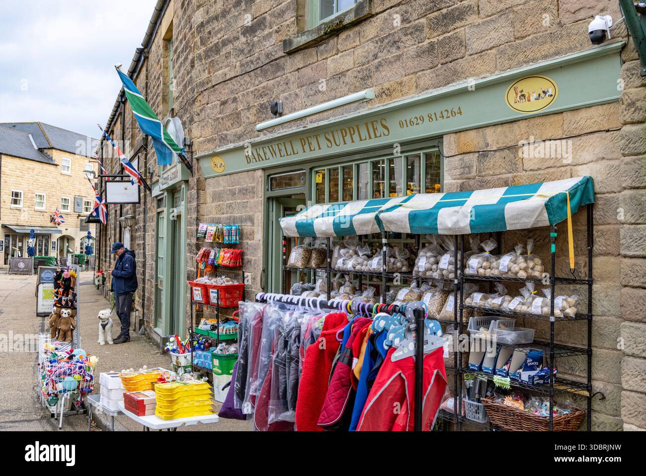 Stadtzentrum von Bakewell, Tierhandelsbedarf in der Wasserstraße Bakewell, Mann, der seinen Hund vor dem Tierhandeladen in England, Großbritannien führt Stockfoto