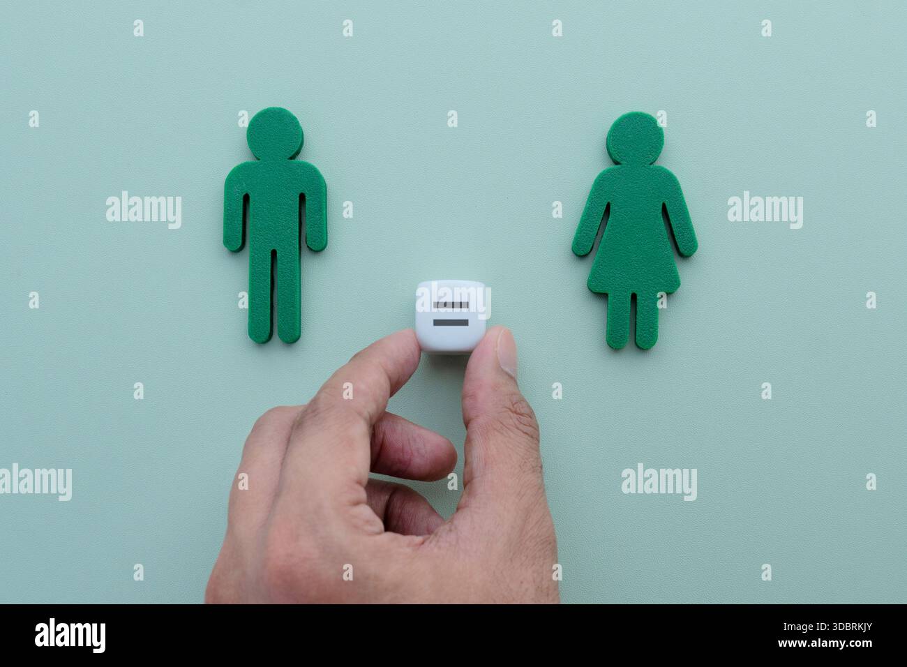 Eine Hand platziert einen weißen Würfel mit einem Gleichheitszeichen zwischen grünen männlichen und weiblichen Figuren. Gleichstellung der Geschlechter, faire Rechte, Ausgewogenheit und Chancengleichheit Stockfoto