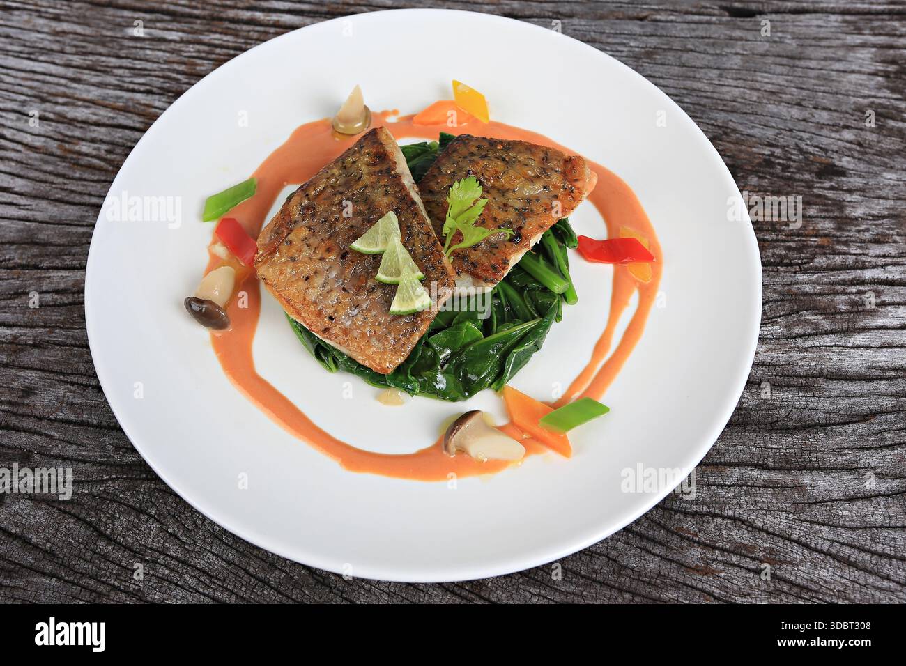 Seebarschsteak serviert mit Salat, gewürzt mit Olivenöl und Zitronenscheiben Stockfoto