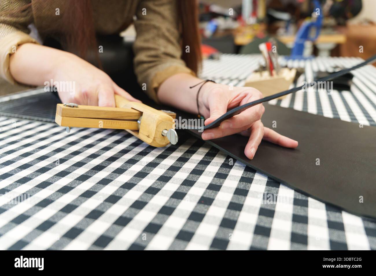 Lederhandwerker mit einem Holzschneider zum Schneiden präziser Streifen aus einem schwarzen Lederblatt. Hochwertige Fotos Stockfoto