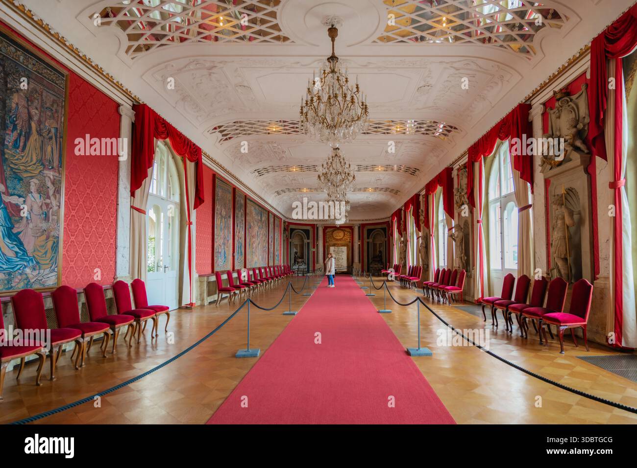 Sigmaringen, Deutschland - 09. September 2025: Blick auf einen langen Saal im Hohenzollernschloss mit rotem Teppich, Wänden, Stühlen und Vorhängen und Chandeli Stockfoto