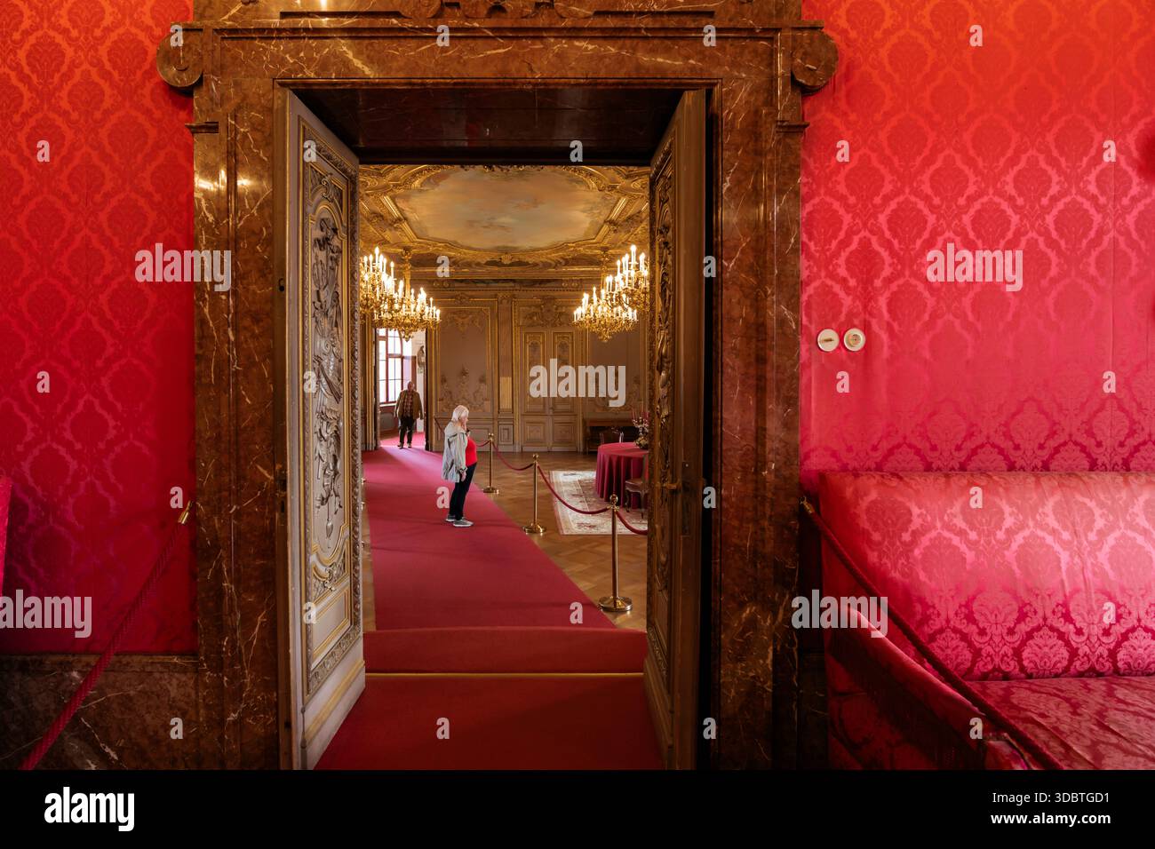 Sigmaringen, Deutschland - 09. September 2025: Blick auf das opulente Innere des Hohenzollernschlosses, wo karmesinrote Mauern auf goldene Kronleuchter treffen Stockfoto