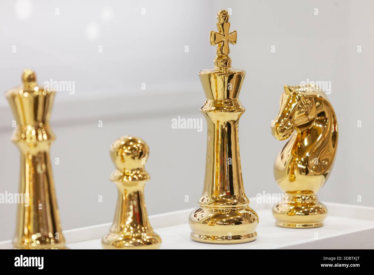 Eine Nahaufnahme von vier polierten goldenen Schachfiguren, darunter eine Königin, ein Bauernhof, ein König und ein Ritter, die auf einer weißen Oberfläche stehen Stockfoto
