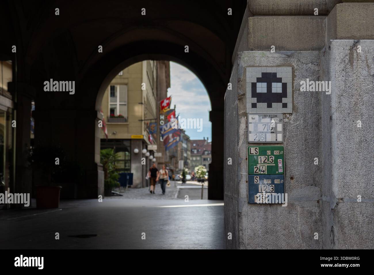 Space Invader Fliesenmosaik auf einer Steinmauer unter einem Berner Torbogen mit Fußgängern in der historischen Altstadt Stockfoto