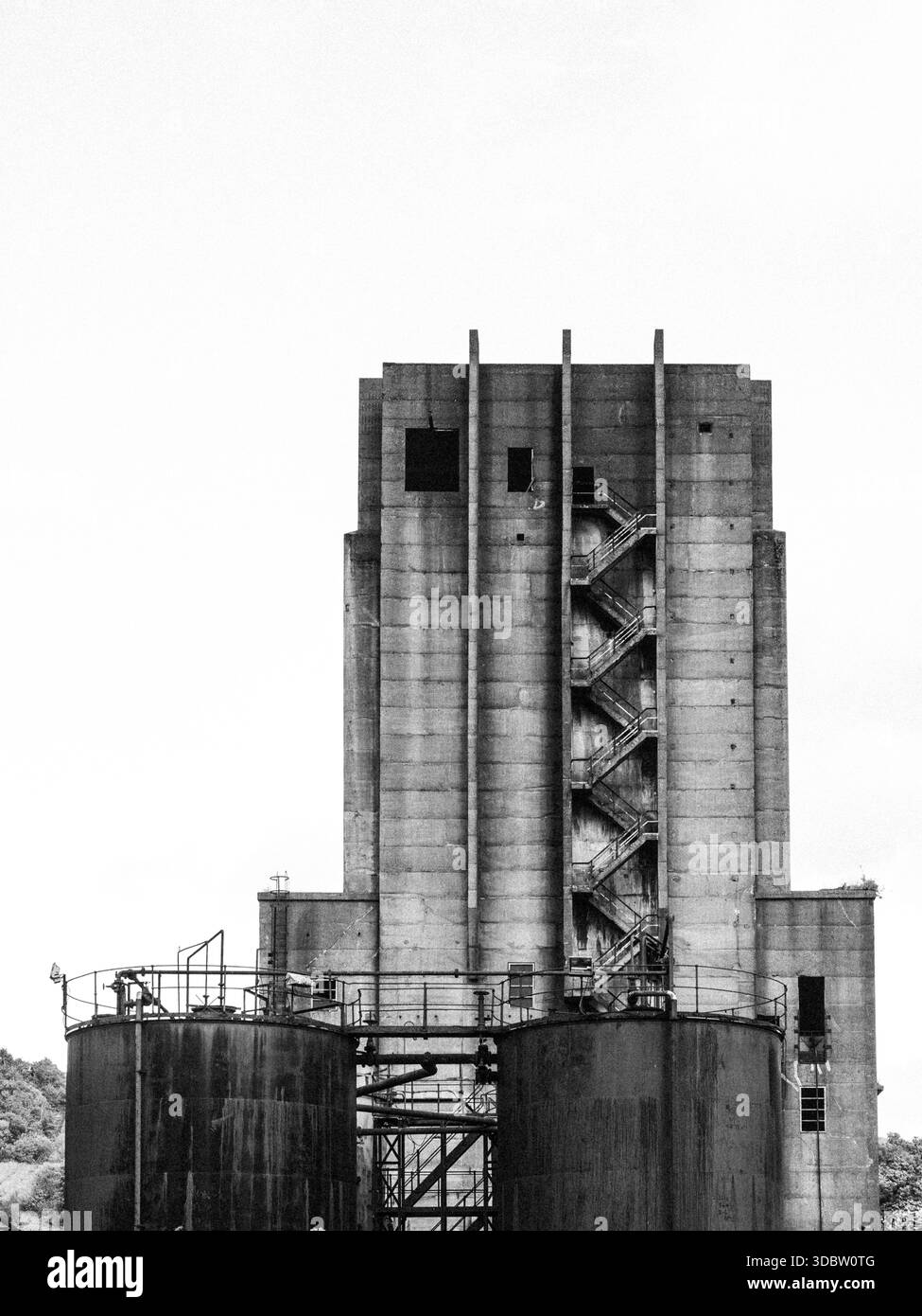 Verlassener Betonsilo-Turm mit externer Zickzack-Treppe und verrosteten Lagertanks - schwarz-weiße Industriearchitektur Stockfoto