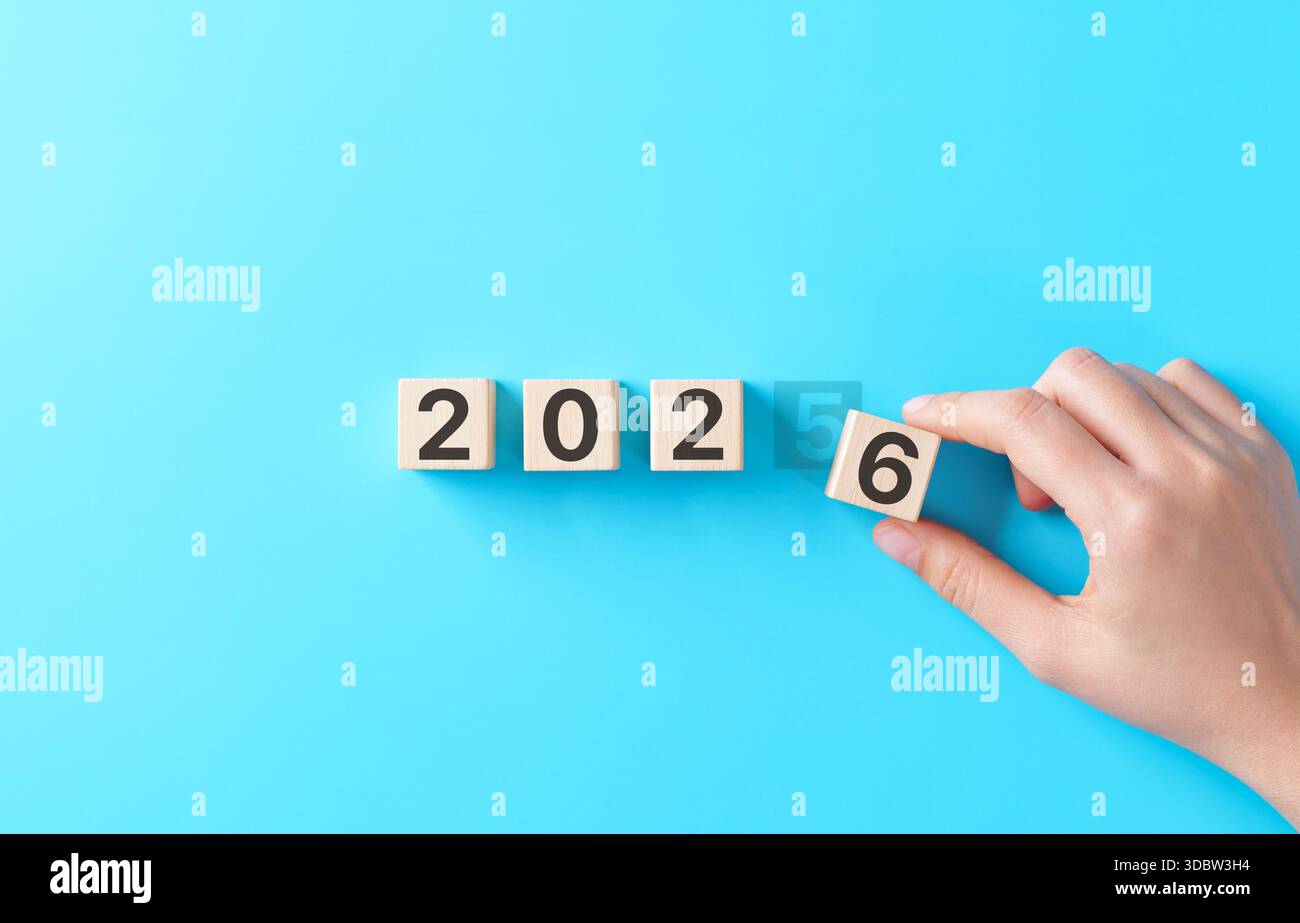 Neujahr- und Zukunftsplanung. Handwechselnder Holzblock von 2025 bis 2026 auf blauem Hintergrund, symbolisiert Neuanfang, Geschäftsziele, Vision Stockfoto
