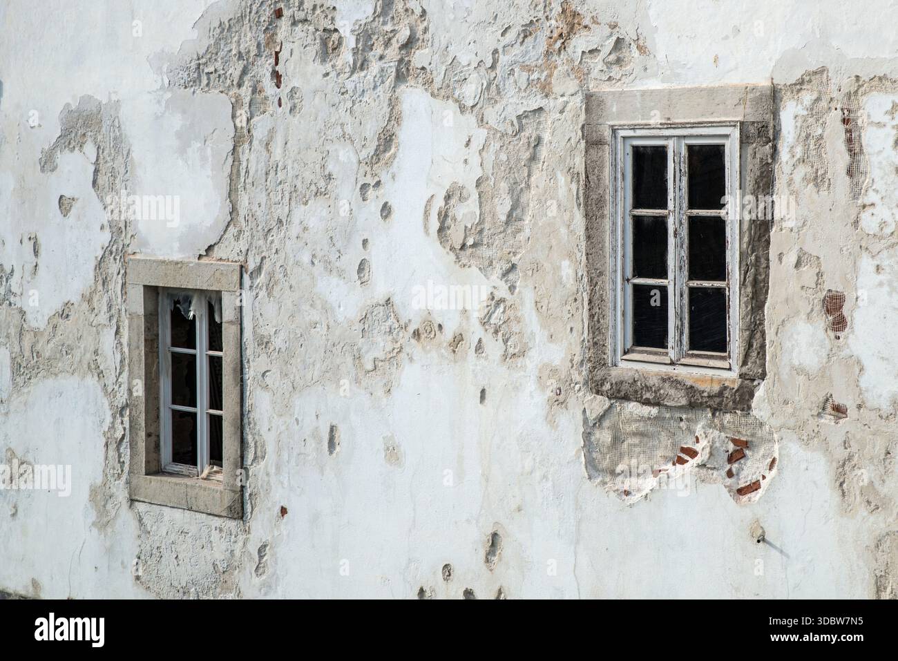 Zwei Fenster in einer alten und beschädigten Putzmauer eines Gebäudes in der Stadt Tavira, Algarve, Portugal Stockfoto