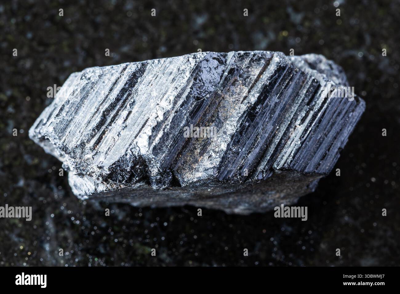 Probe von rohem schwarzem Turmalin-Schorl-Mineral auf schwarzem Granithintergrund aus nächster Nähe Stockfoto