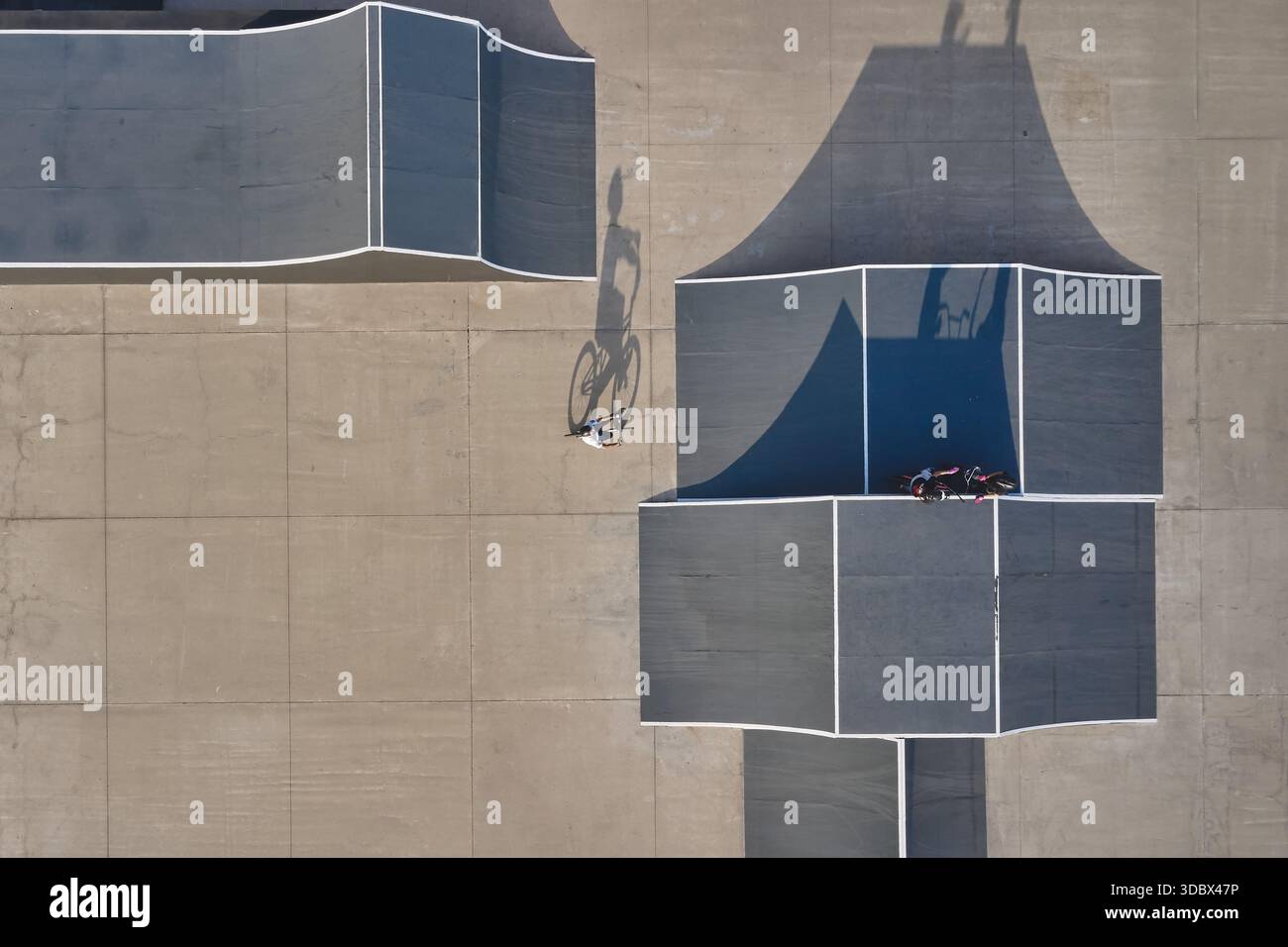 Biker, der Tricks in einem urbanen Skatepark mit Rampen und Schatten macht Stockfoto