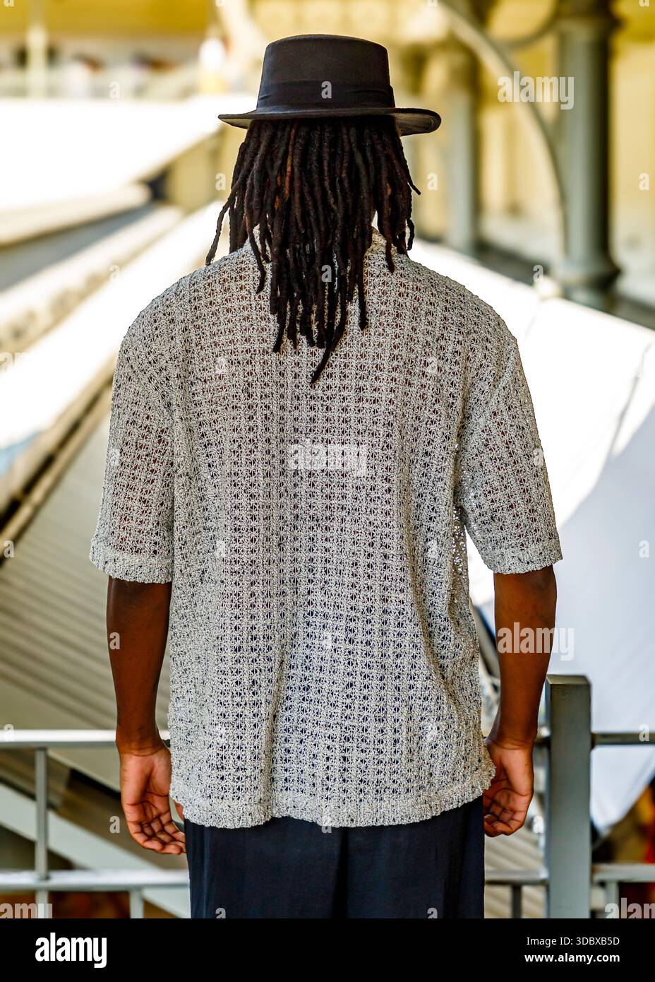 Eine Person mit Dreadlocks, die einen Hut und ein helles Hemd trägt, steht mit dem Rücken zur Kamera. Stockfoto