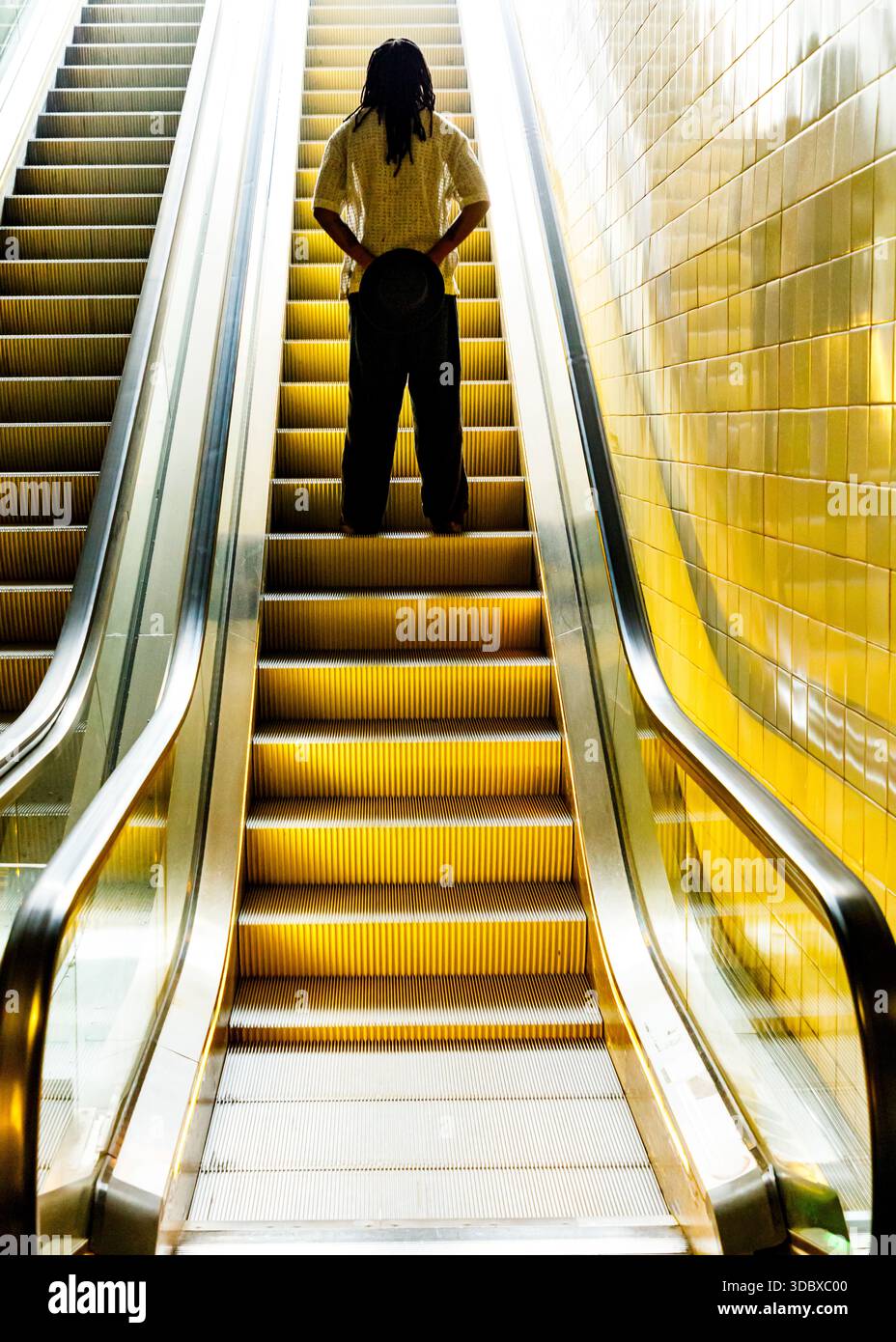 Eine Person steht auf einer Rolltreppe und hält einen Hut hinter dem Rücken. Stockfoto