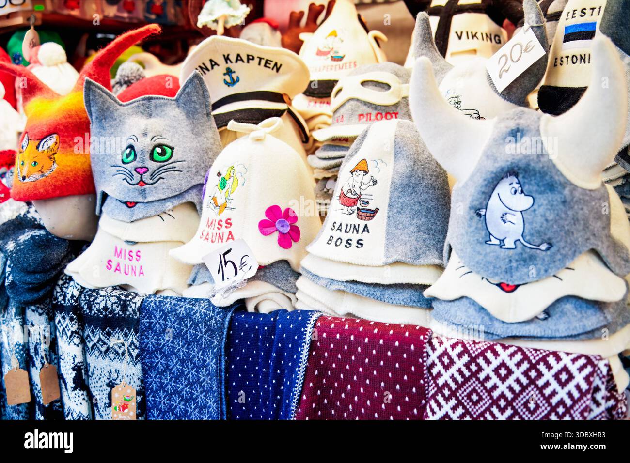 Tallinn, Estland - 03. Dezember 2025: Saunahüte aus Wolle auf dem Weihnachtsmarkt mit lustigen Designs, bunten Mustern, Preisschildern und gestricktem sca Stockfoto