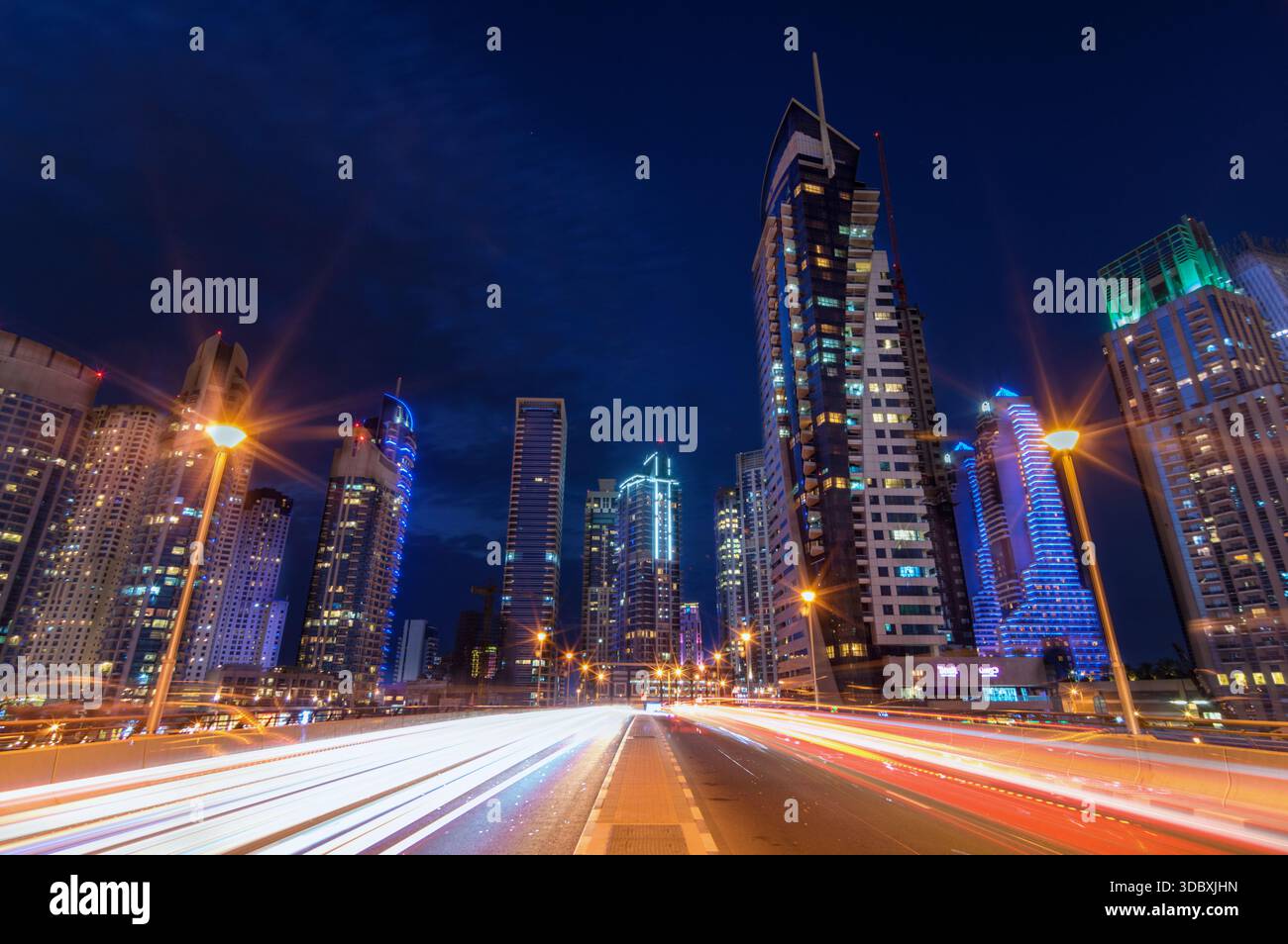Blick auf die pulsierenden Lichtstreifen, die über der Straße verschwimmen und von den hoch aufragenden Wolkenkratzern reflektieren, die den tiefblauen Himmel durchdringen, Dubai, United AR Stockfoto