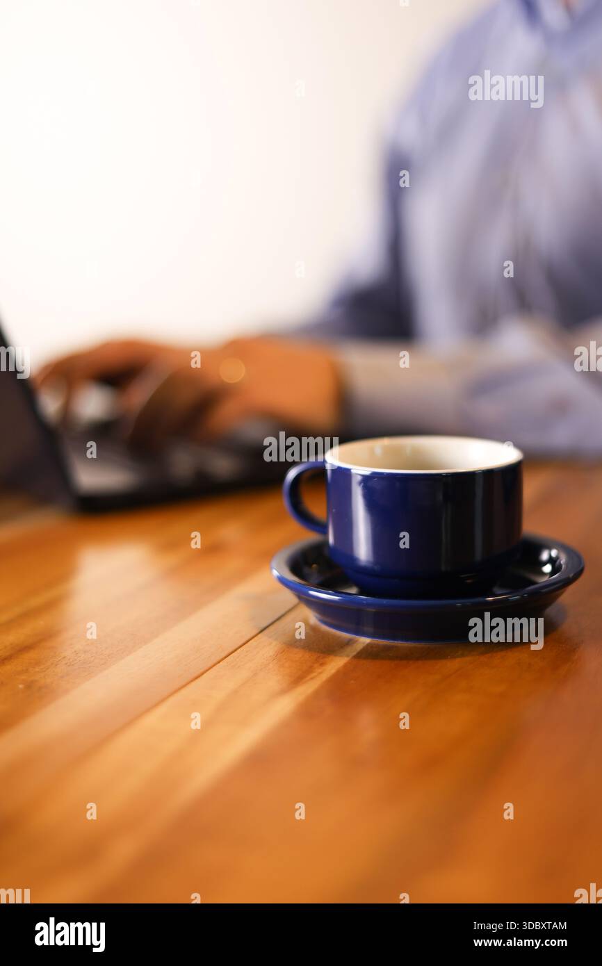 Flache Tiefe des Field Coffee Bechers mit der Eingabe eines Mannes auf dem Laptop Stockfoto