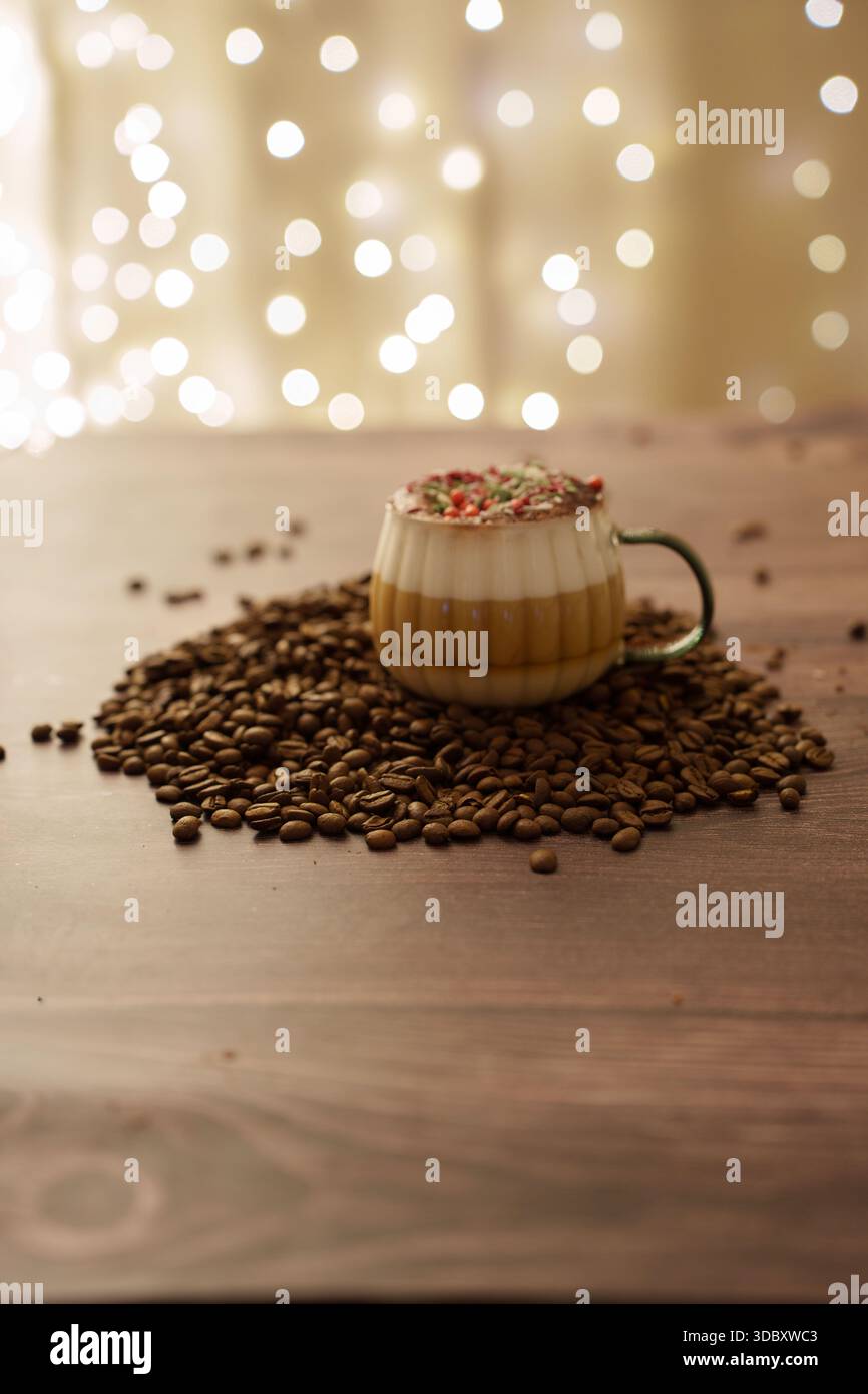 Warme, gemütliche Kaffeeszene mit einem schäumenden Becher, umgeben von Kaffeebohnen und einem weichen, hellen Bokeh-Hintergrund, der eine festliche und einladende Atmosphäre auf einem schafft Stockfoto