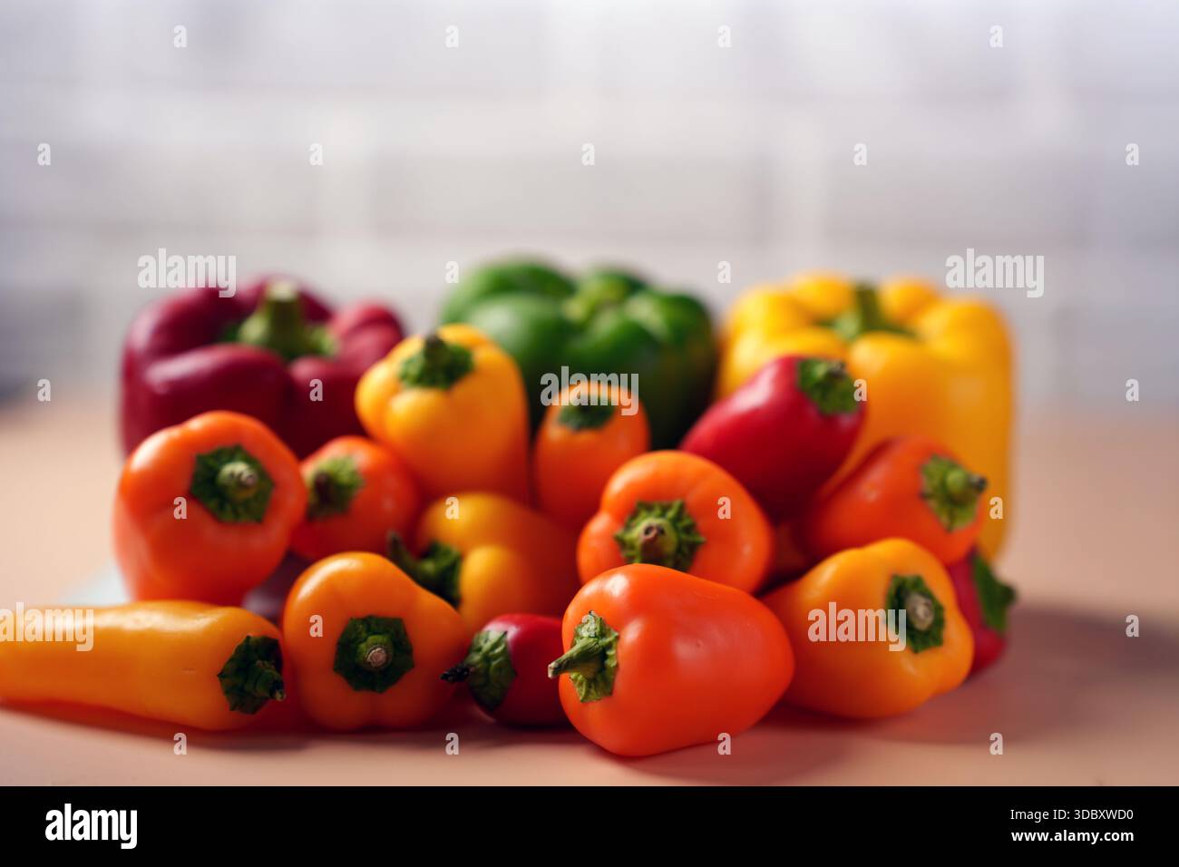 Lebendige Auswahl an roten, gelben und grünen Paprika auf einer weichen neutralen Oberfläche mit unscharfem Hintergrund, die Frische und Farben hervorhebt Stockfoto