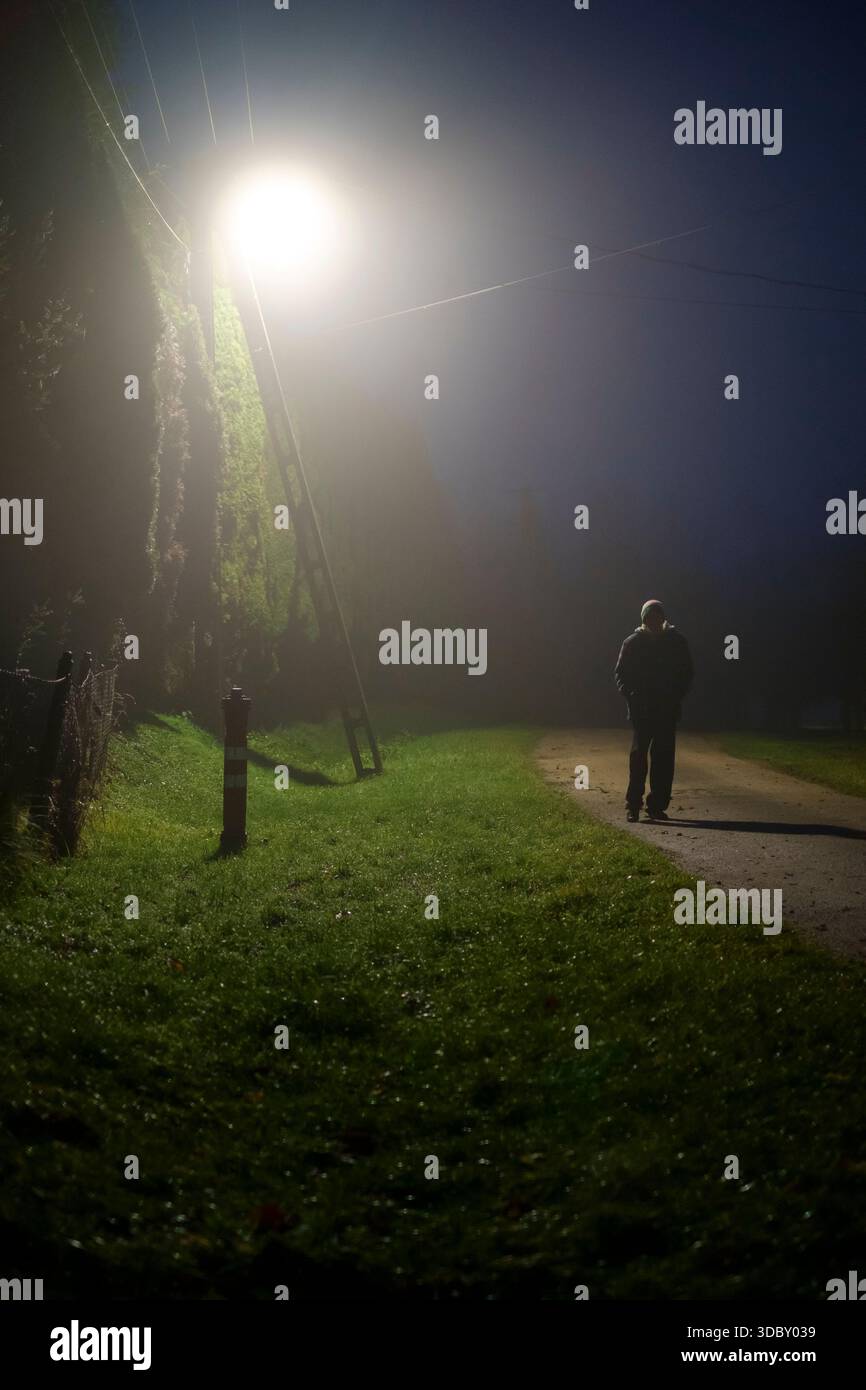 Älterer Mann, der in der Dunkelheit mit nebligen niedrigen Wolken spaziert, nebelige ländliche Gasse in eisigem Nebel nachts zala County ungarn Stockfoto