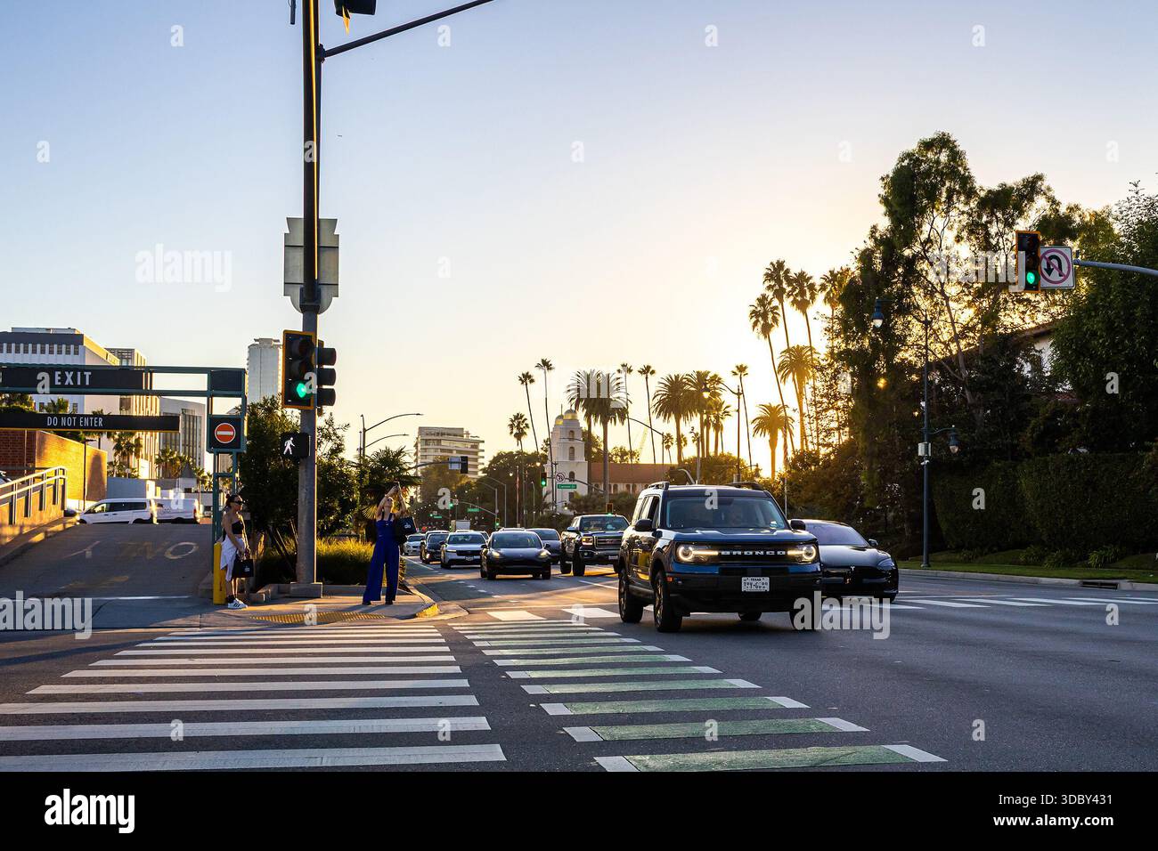 Santa Monica Boulevard und Rodeo Drive bei Sonnenuntergang mit Autos auf der berühmten Straße in Beverly Hills, Los Angeles, mit hinterleuchteten Palmen Stockfoto