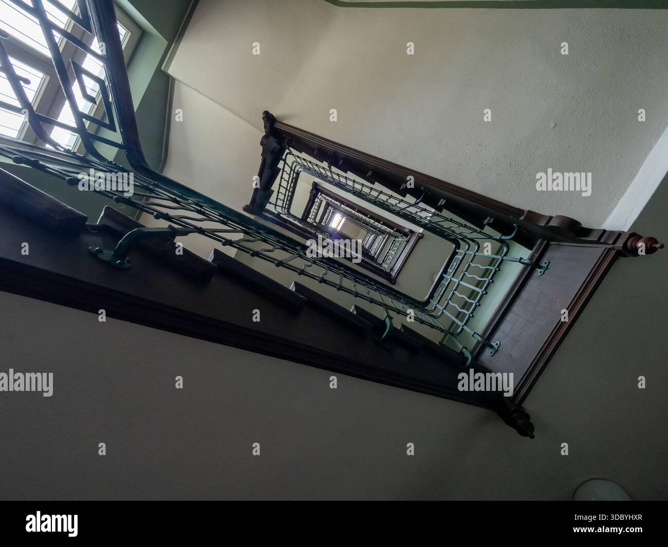 Vintage-Jugendstiltreppe in München - kunstvolle schmiedeeiserne Balustrade und Holzgeländer mit starker vertikaler Perspektive Stockfoto