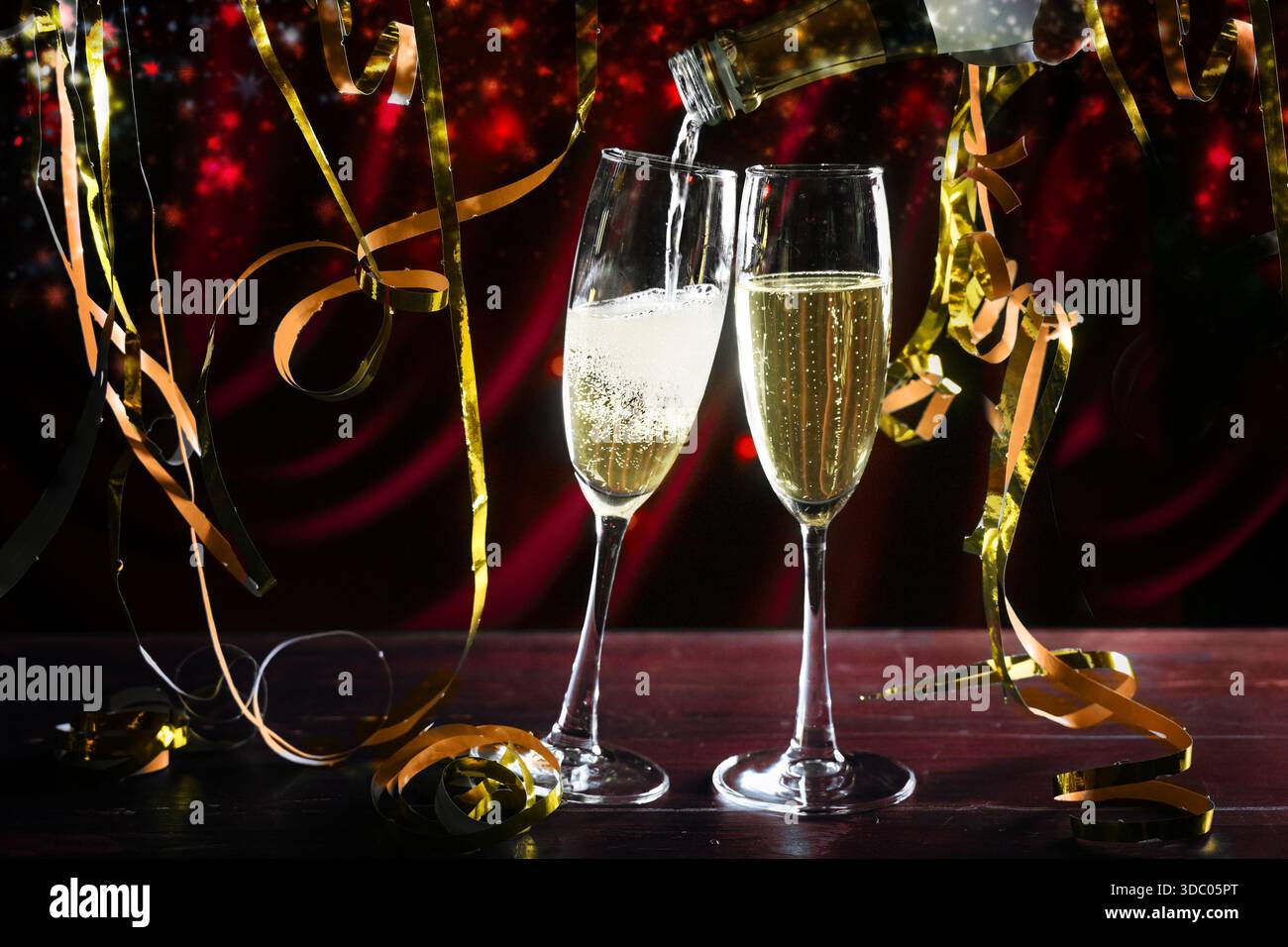Zwei Sektgläser werden gefüllt, goldene Streamer und ein dunkelroter Hintergrund mit Reflexen, Party für zwei an Feiertagen, Neujahr oder Nachtleben Stockfoto