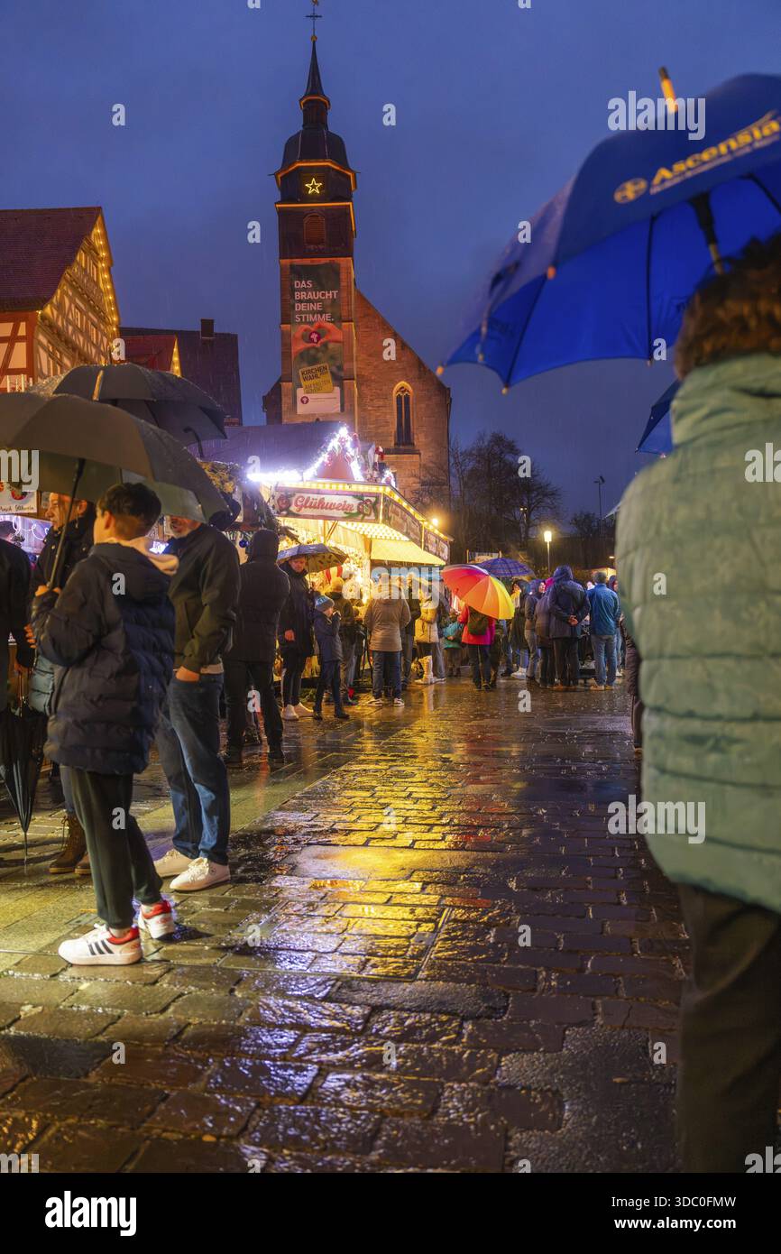 Menschen mit Sonnenschirmen auf einem nassen Weihnachtsmarkt bei Nacht mit beleuchteter Kirche im Hintergrund, Weihnachtsmarkt Böblingen, Deutschland Stockfoto
