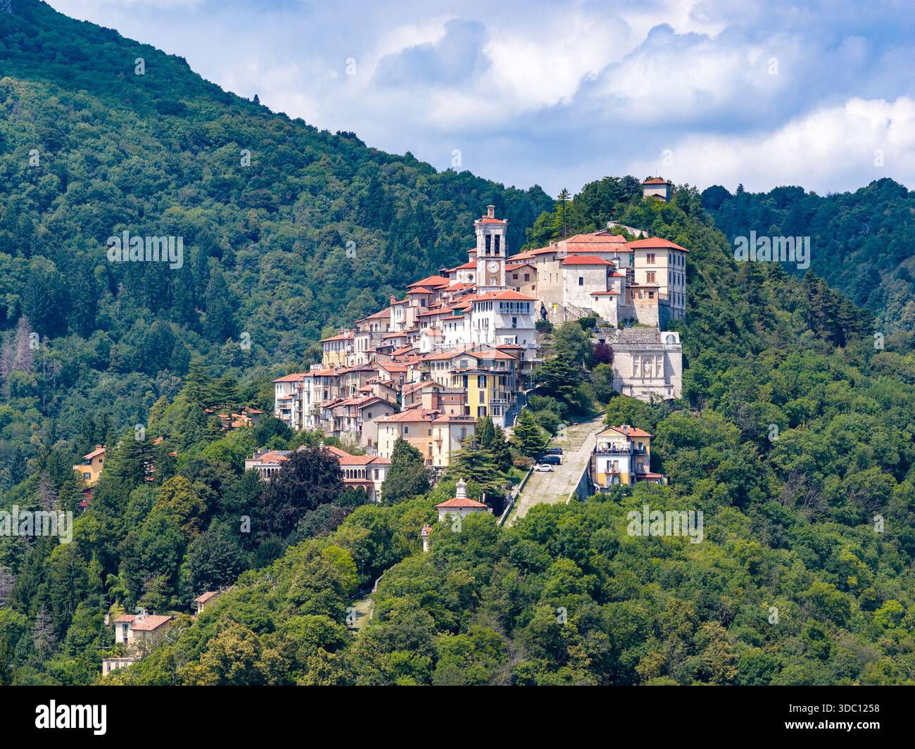 Blick aus der Vogelperspektive auf ein Dorf auf einem Hügel in der Nähe von Varese, Italien, umgeben von einem Kirchturm und Steinhäusern über dichten Wäldern. Stockfoto