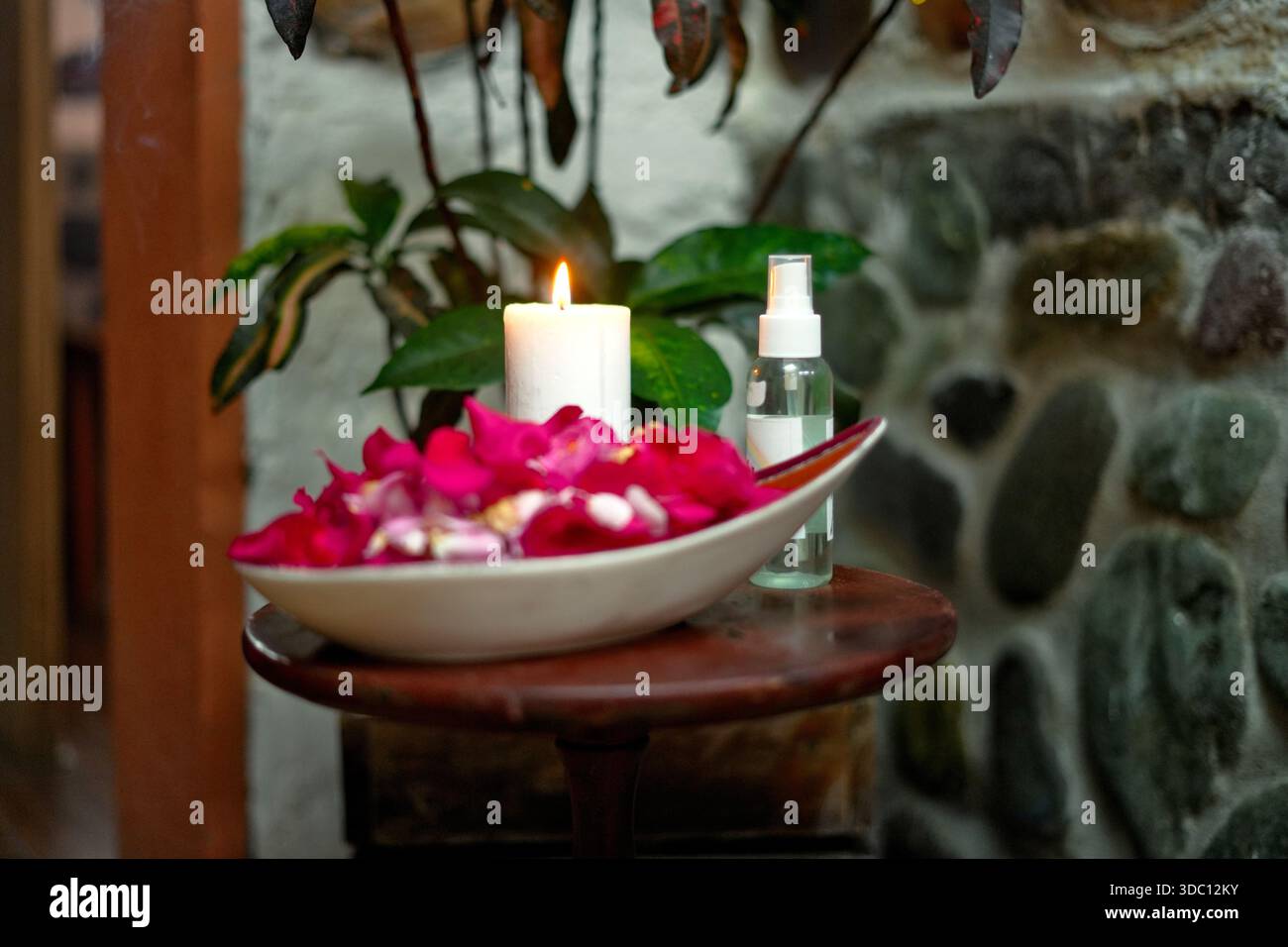 Spa-Behandlungen mit brennender Kerze, Rosenblüten in einer Schüssel und Sprühflasche auf einem Holztisch schaffen eine ruhige Atmosphäre Stockfoto