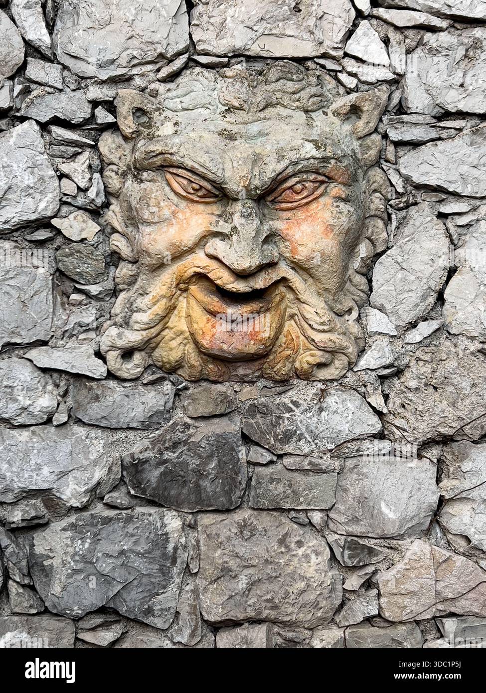 Die mythologische Teufelskulptur ziert eine verwitterte, rustikale Steinmauer Stockfoto