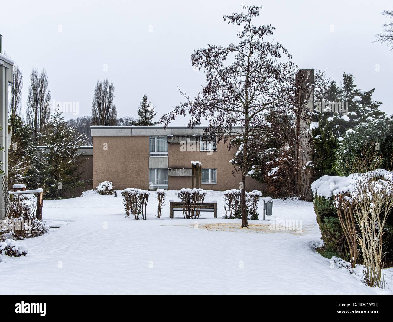 Schneebedeckter Innenhof mit Bank und Appartementgebäude an einem bewölkten Wintertag Stockfoto