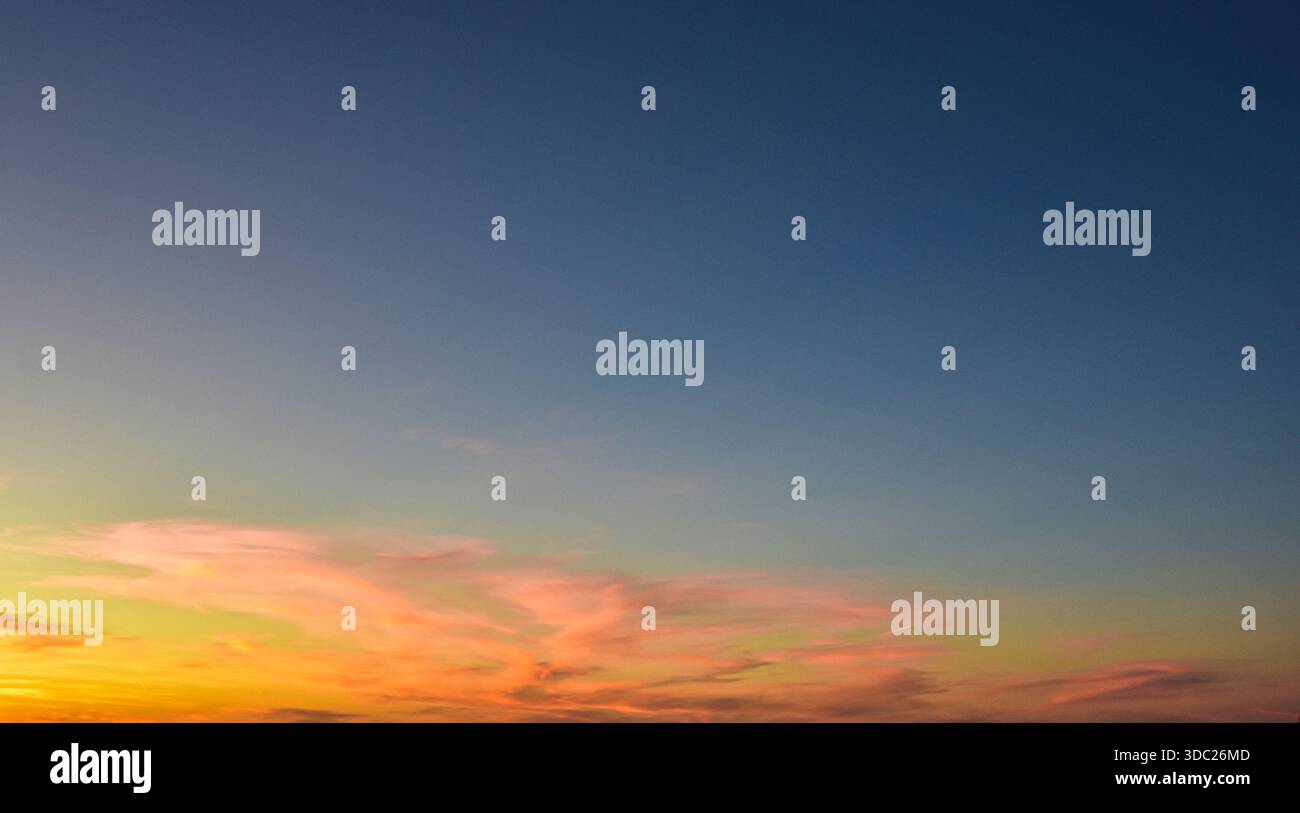 Einfache Himmelskomposition mit warmen Sonnenuntergangsgradienten und zarten Wolken, die einen beruhigenden und modernen atmosphärischen Hintergrund bieten. Stockfoto