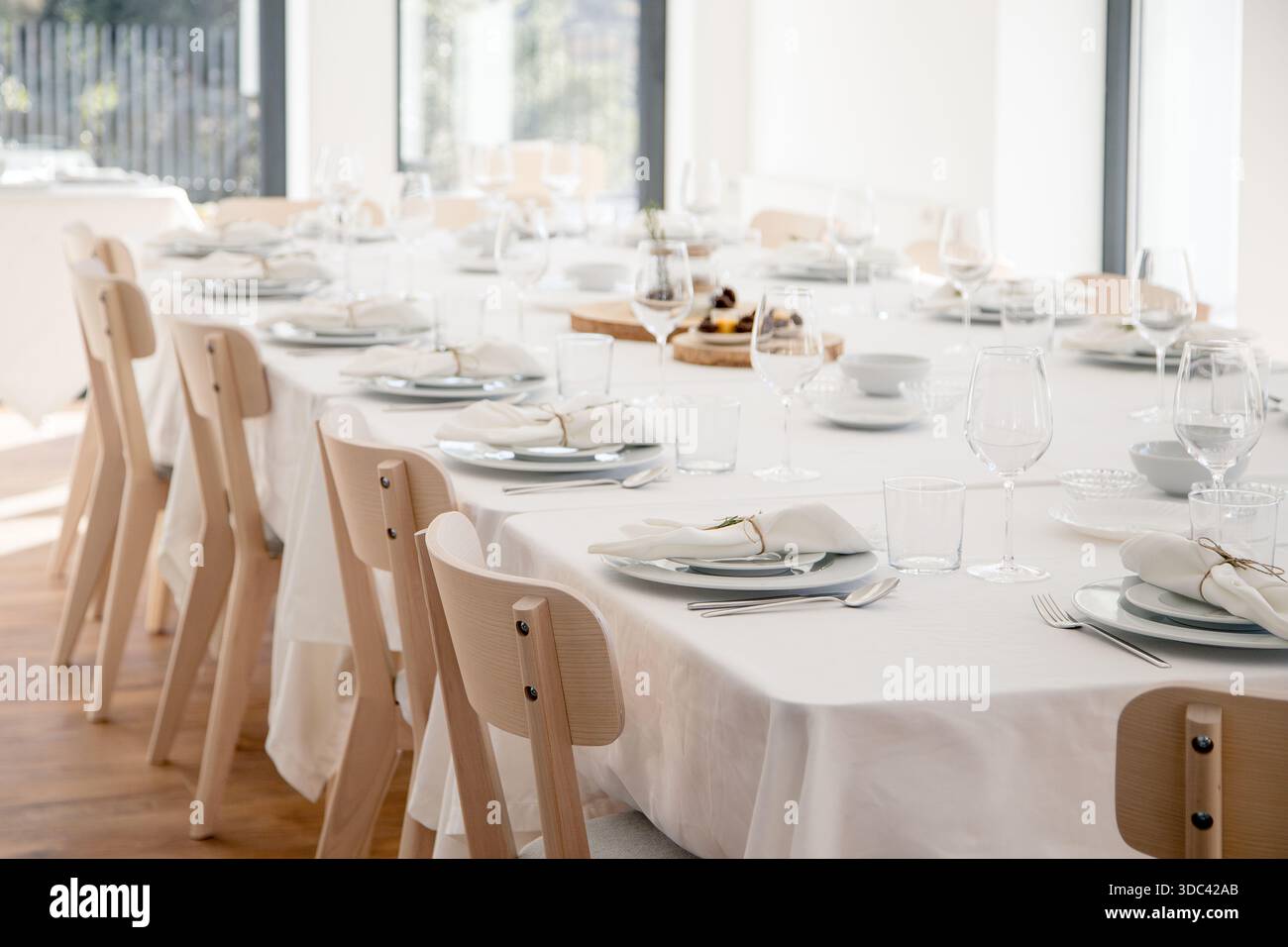 Ein heller, eleganter Speisesaal mit einem langen, weißen Tisch ist für festliche Treffen vorbereitet Stockfoto