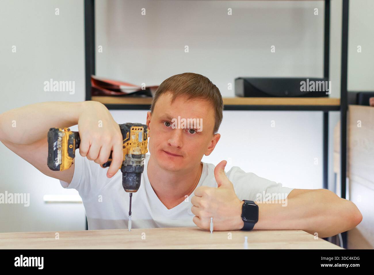 Positiver Mann, der die Daumen hochgibt, mit einem Bohrschrauber auf Holzoberfläche im Projekt zur Verbesserung des Hauses. Stockfoto