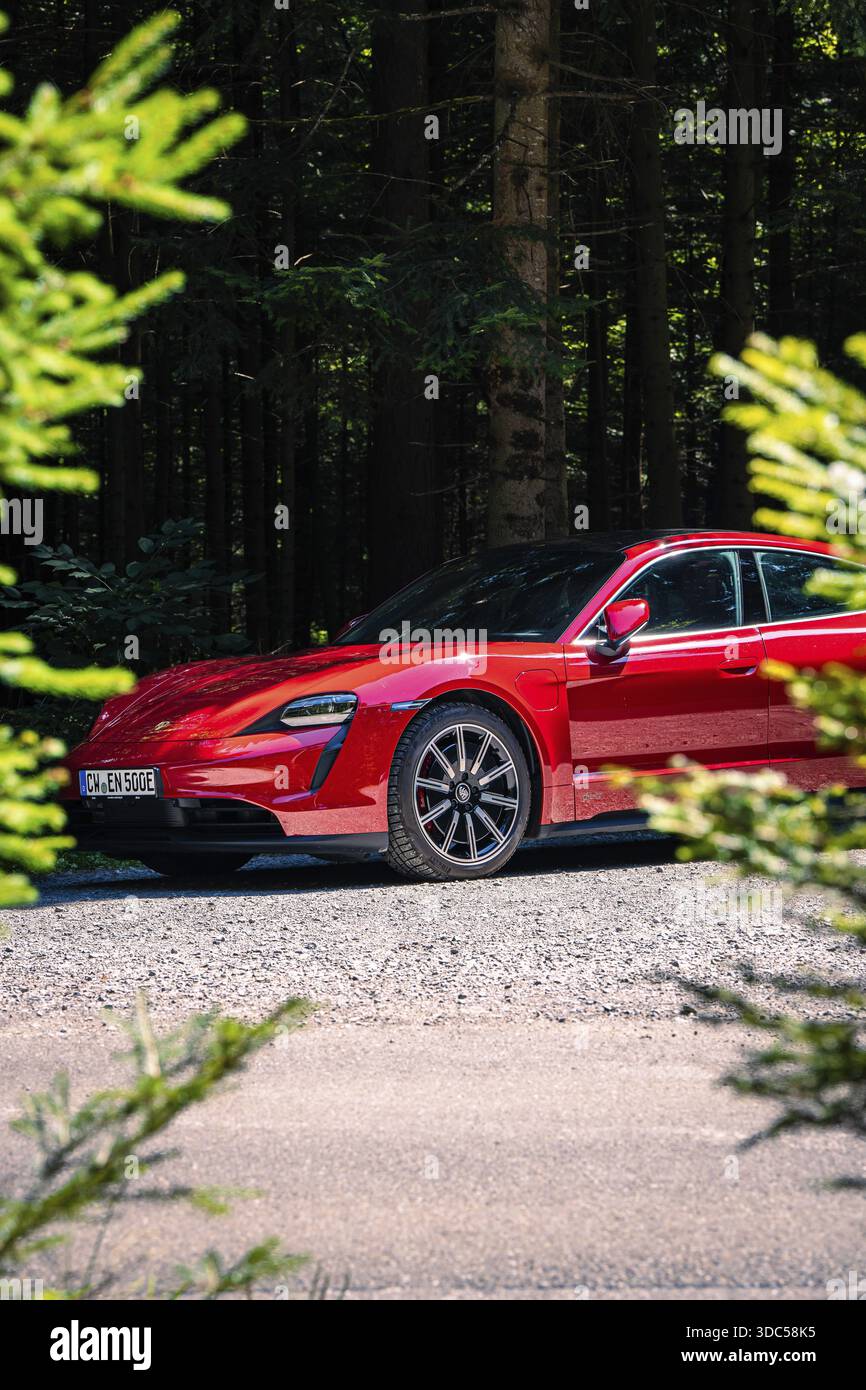 Rotes Auto parkt auf einer Forststraße mit Bäumen im Hintergrund, Porsche Taycan, Hirsch Carsharing. Calw, Deutschland Stockfoto