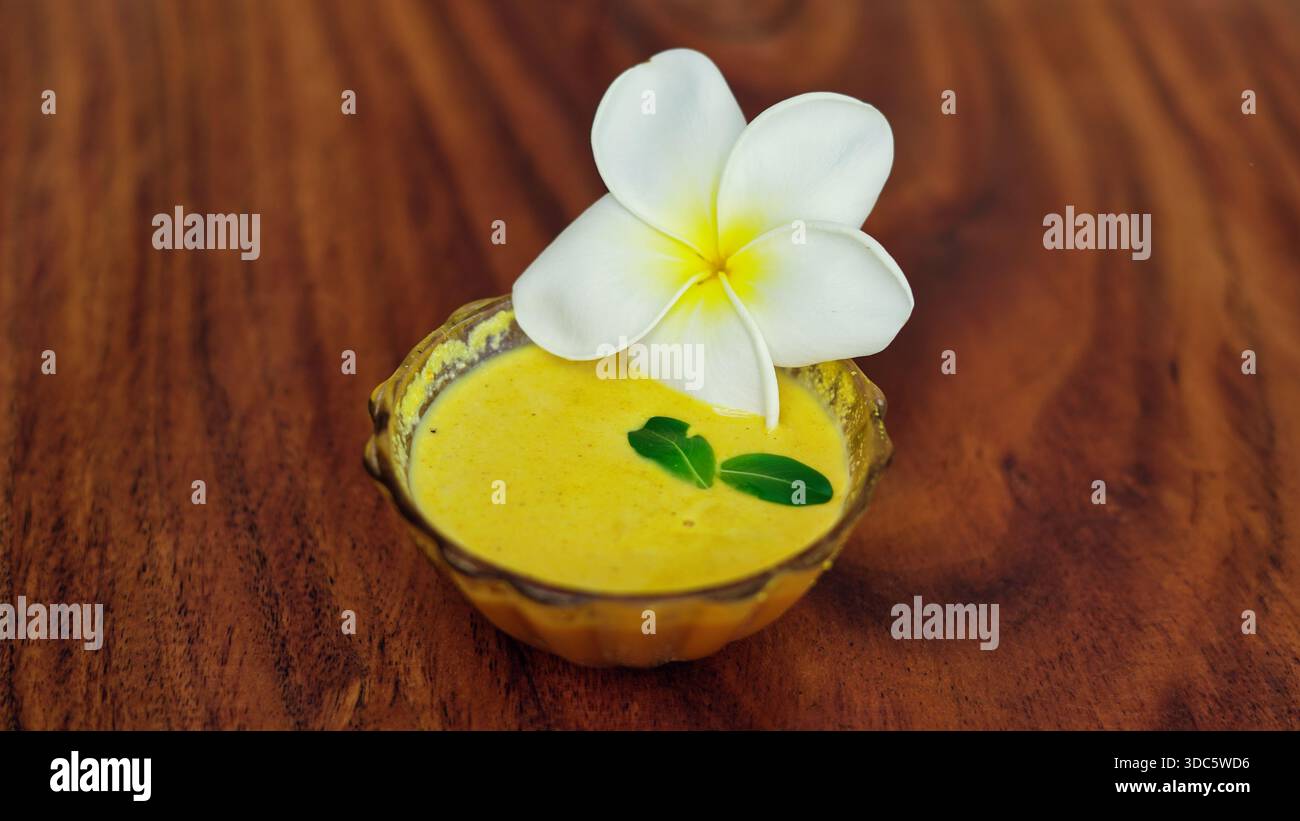 Ubtan- oder ayurvedisches Körperpeeling für glänzende Haut in einer Schüssel auf hölzernem Hintergrund. Traditionelle handgemachte Schönheitsbehandlung mit haldi, Milch, Rosenwasser platziert Stockfoto