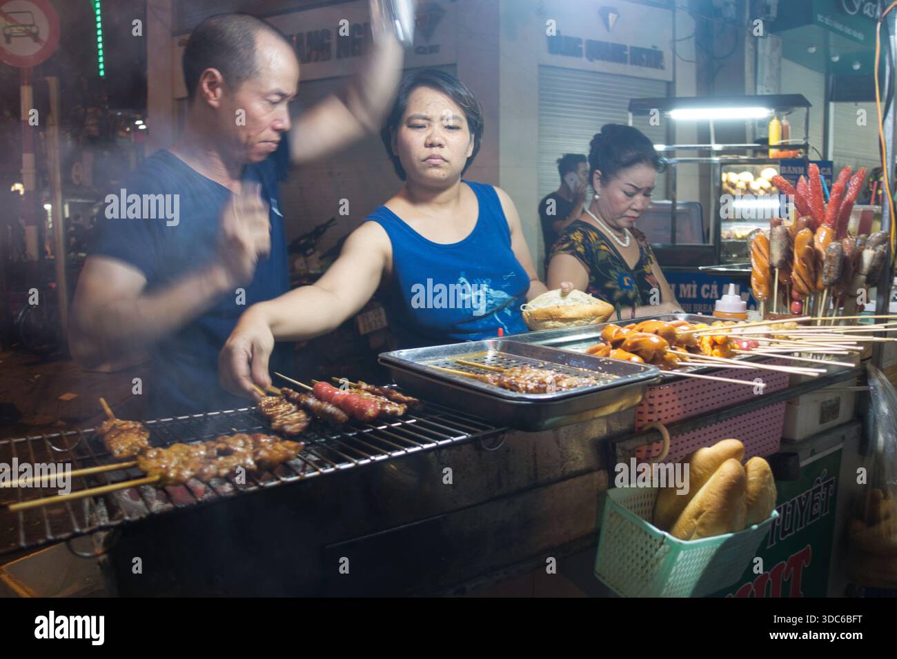 hanoi-Vietnam-10. August 2019, Hanoi, Vietnam. Straßenhändler bereiten gegrillte Spieße und Bánh Mì-Würstchen an einem von Neonlichtern beleuchteten Stand zu Stockfoto