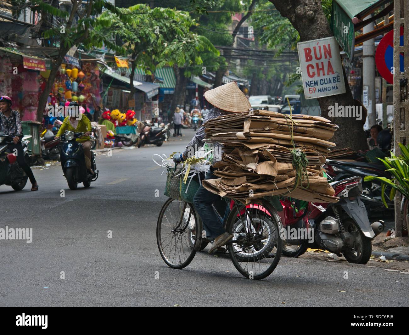 Haoi-10. August 2019, Ein Recycler mit konischem Hut transportiert eine große Ladung gebündelter Pappe auf einem Fahrrad entlang der Hàng MÃ-Straße in der Alten Quarte Stockfoto