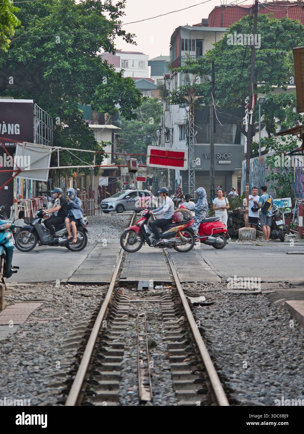 hanoi-Vietnam-10. August 2019: Motorradfahrer fahren an der Bahnüberquerung in einem überfüllten Stadtgebiet von Hanoi, Vietnam. Spiegelt das wahre wider Stockfoto