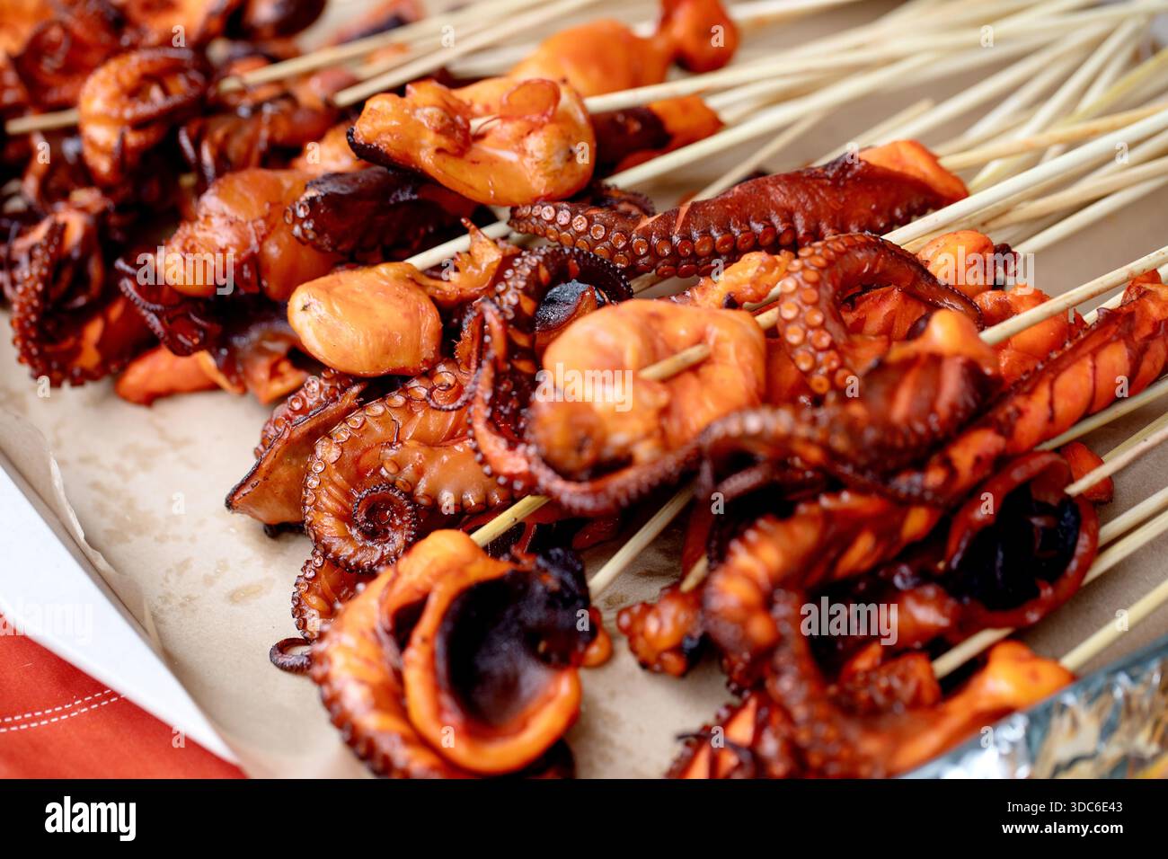 Nahaufnahme von gegrilltem Baby-Oktopus auf Holzspießen. Fisch- und Meeresfrüchte-Barbecue mit verkohlten Oktopusstücken mit Tentakelstruktur. Mediterrane Küche St Stockfoto
