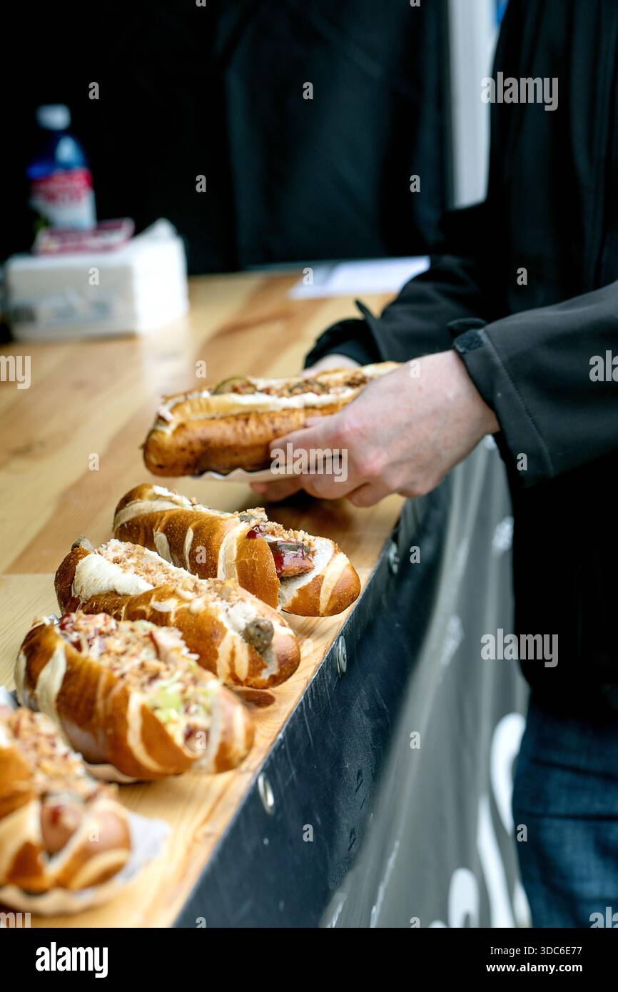 Person in dunkler Jacke, die Sandwich von Holztheke auswählt. Frisch gefüllte Baguettes mit verschiedenen Belägen, Café-Einstellung. Streetfood bereit Stockfoto