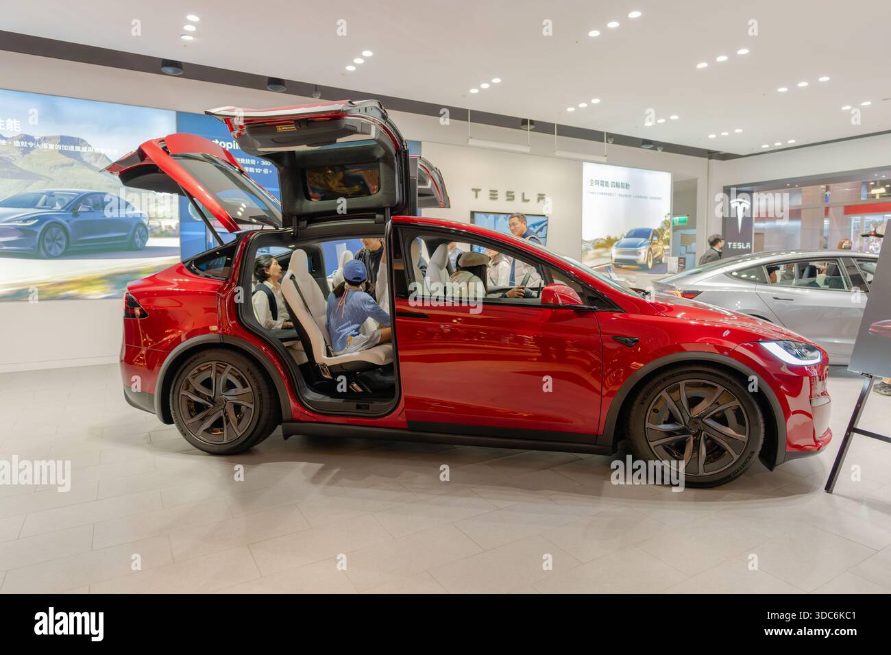 Taipei, Taiwan – 20. Dezember 2025: Roter Tesla Model X mit Falken-Flügeltüren im Ausstellungsraum geöffnet, während Kunden das Fahrzeug inspizieren Stockfoto