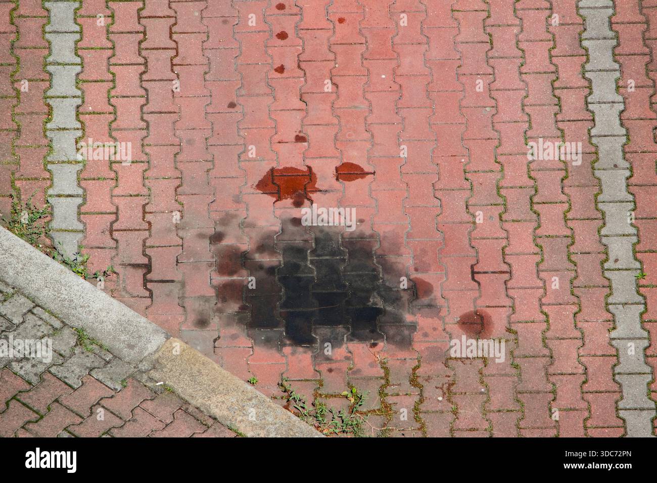 Ölfleck auf leerem roten Kopfsteinpflasterparkplatz Stockfoto