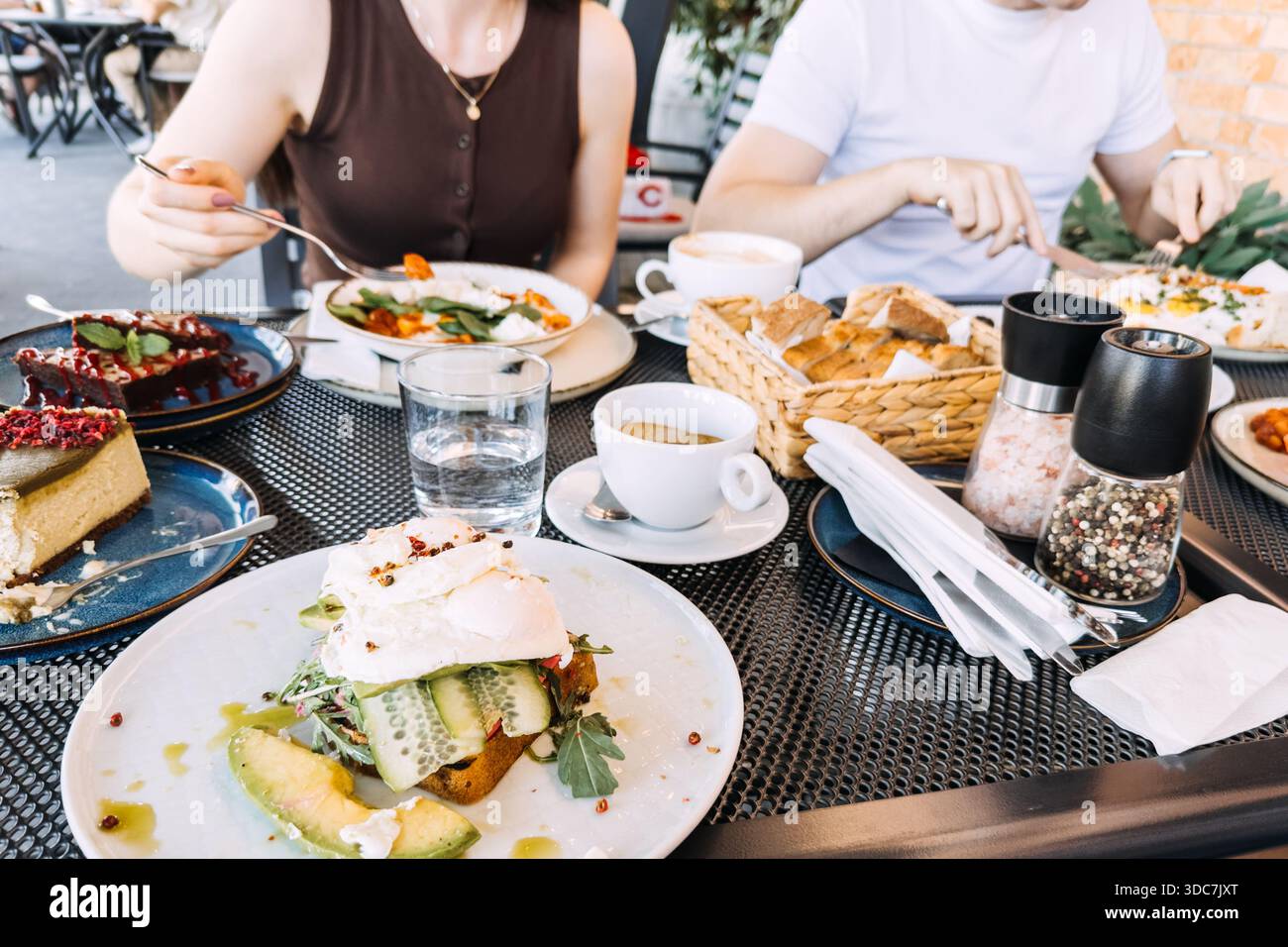 Die Leute teilen sich ein Gourmet-Frühstück am Café-Tisch im Freien. Lifestyle-Fotografie, gemeinsame Mahlzeiten, urbane Atmosphäre. Stockfoto