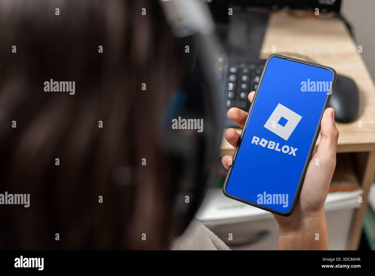 Ein nicht erkennbarer weiblicher Teenager hält ein Handy mit dem Roblox-Logo auf dem Bildschirm mit blauem Hintergrund Stockfoto