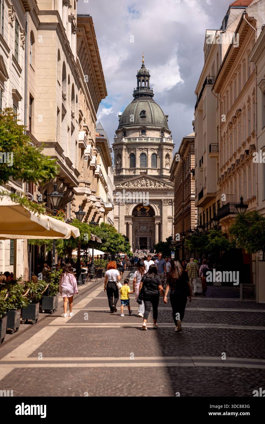 Blick auf die Straße zum Stephansdom in Budapest, Ungarn, mit Fußgängern, die zwischen historischen Gebäuden spazieren. Stockfoto