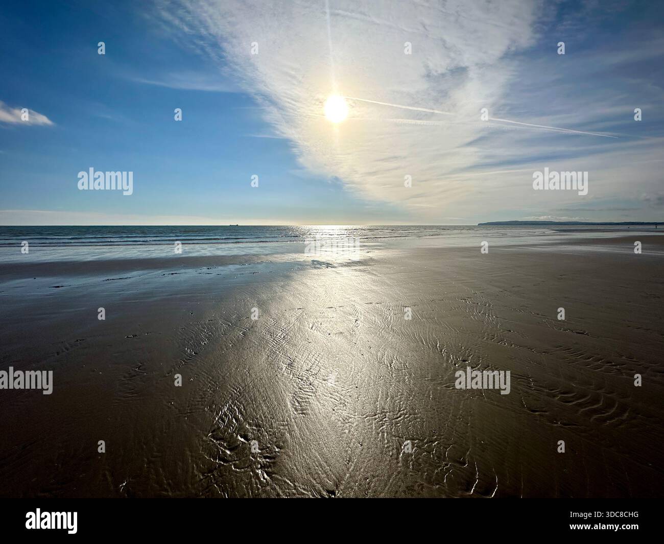 Camber Sands, East Sussex – Sonnenaufgangslicht reflektiert auf nassem Sand, während Wellen auf das ruhige Ufer treffen Stockfoto