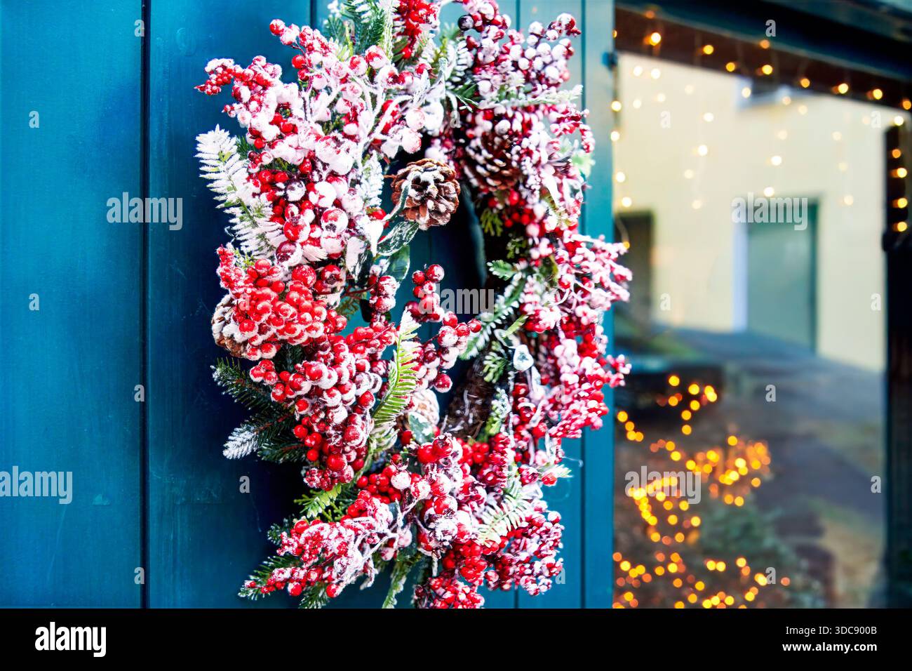 Winterzauber und festliche Textur erscheinen in einem dekorativen Weihnachtskranz mit roten Beeren, Tannenzweigen und Tannenzapfen, die an einer Tür hängen, Glowi Stockfoto